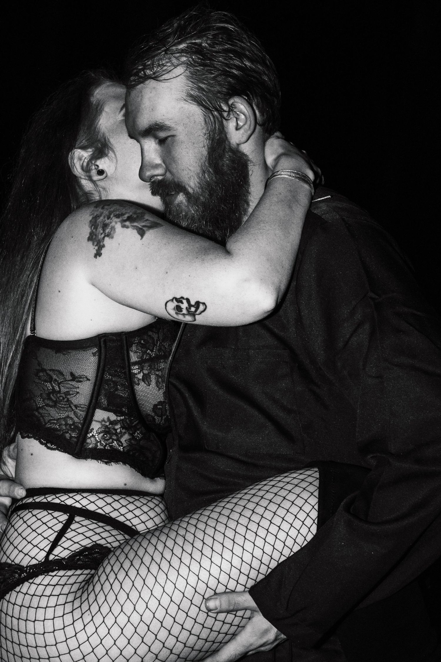 Intimate black and white portrait of couple in romantic embrace wearing dark clothing.