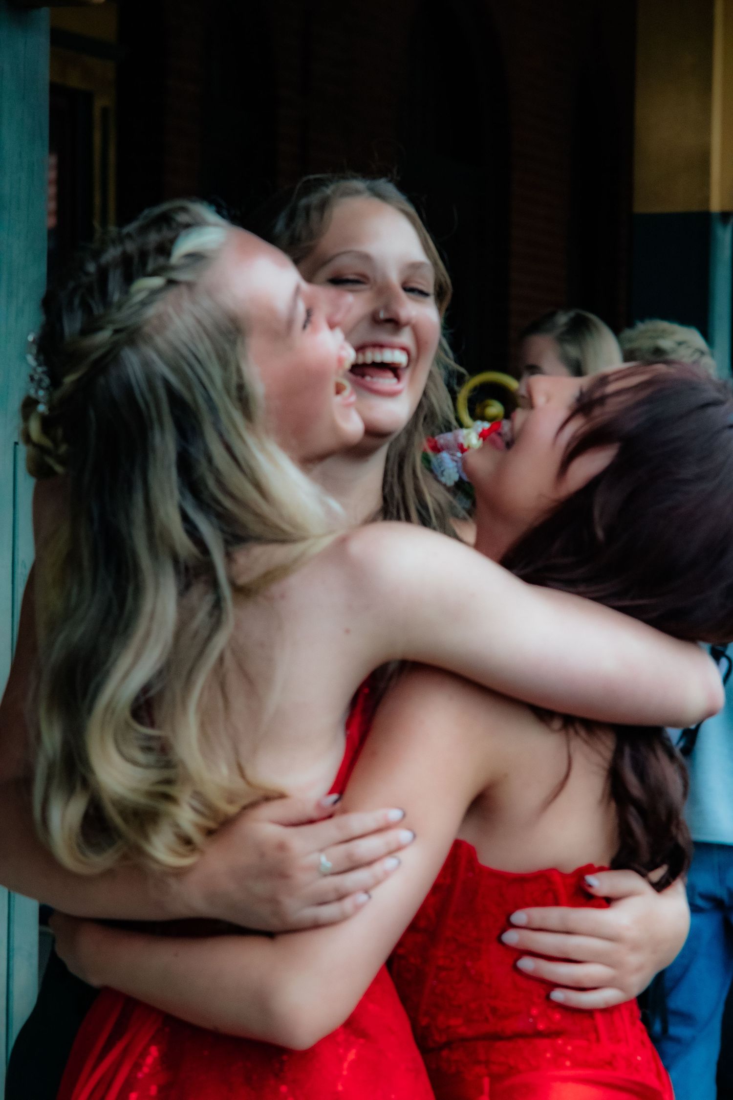 Friends in red dresses share an emotional embrace while laughing together.