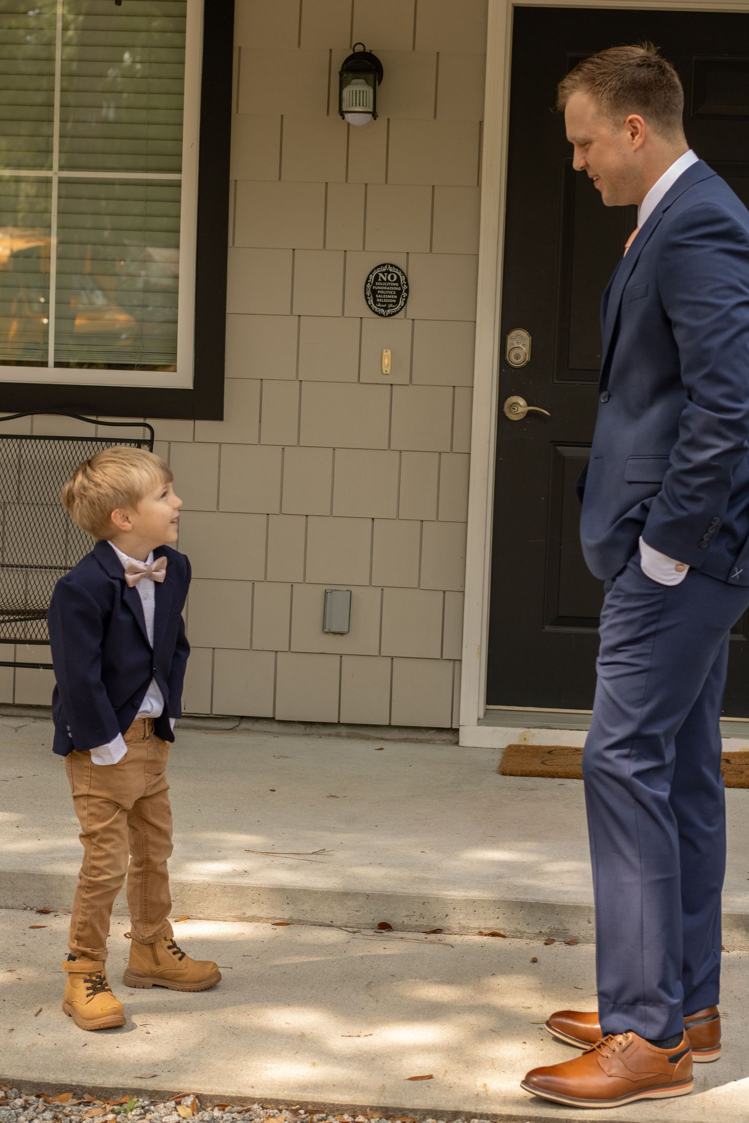 A sweet moment between a suited figure and small child in formal wear on a front porch.