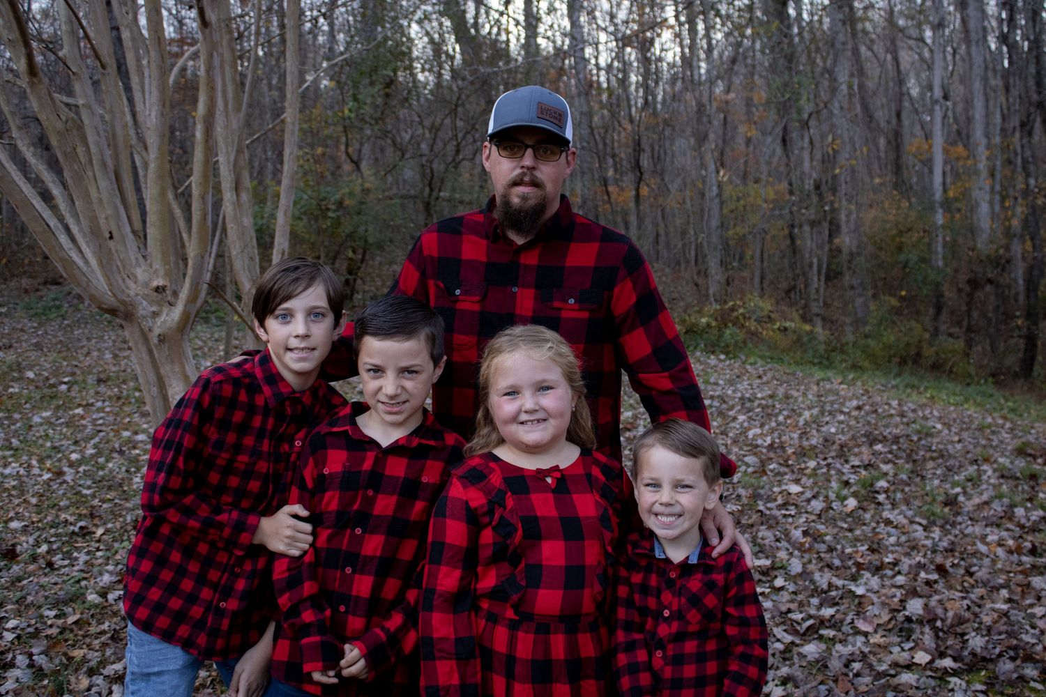 A group in matching red and black buffalo plaid flannel shirts poses together in a wooded autumn setting.