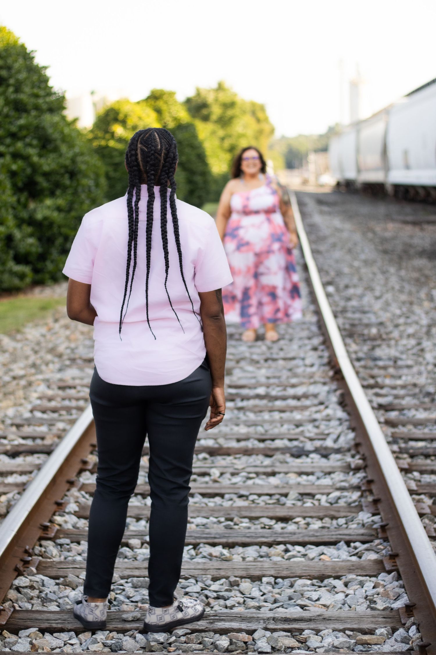 Couple standing on railroad tracks in contrasting pink and black outfits.