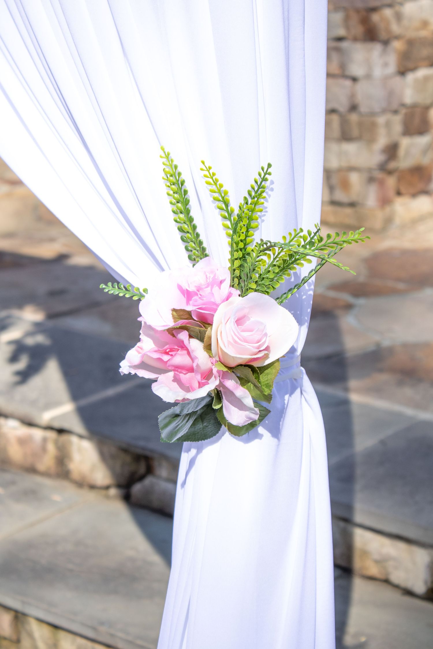 Pink roses and greenery decorating white fabric draped on stone steps at an outdoor venue.