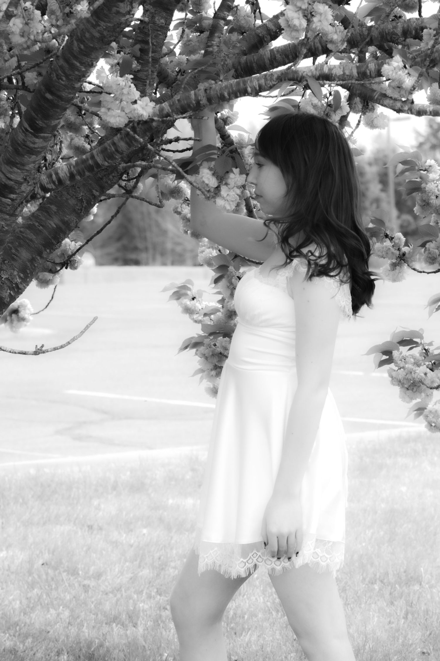 A black and white photo of someone in a white dress standing beside flowering tree branches.