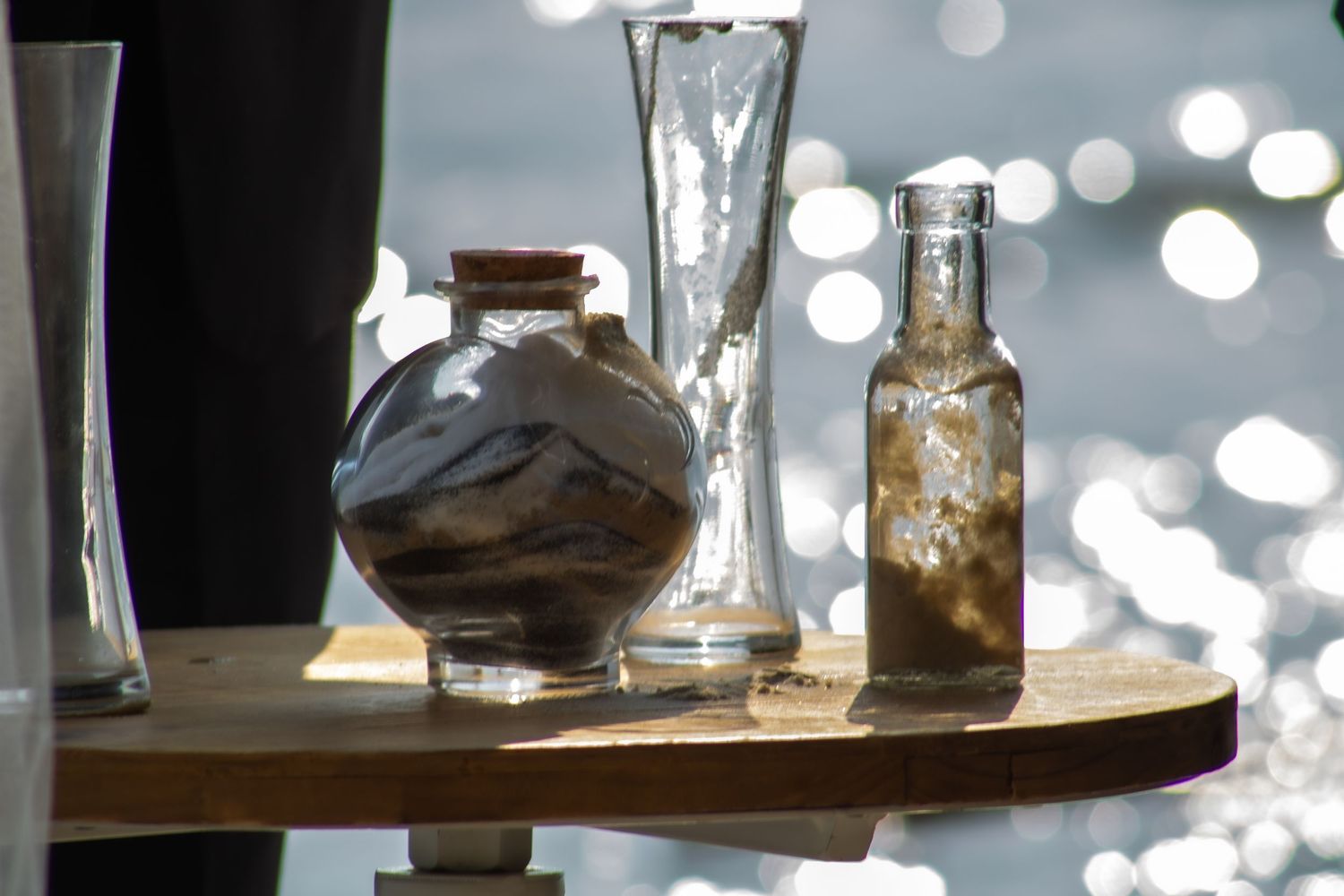 Glass vases and bottles arranged on a wooden surface with bokeh lights in the background.