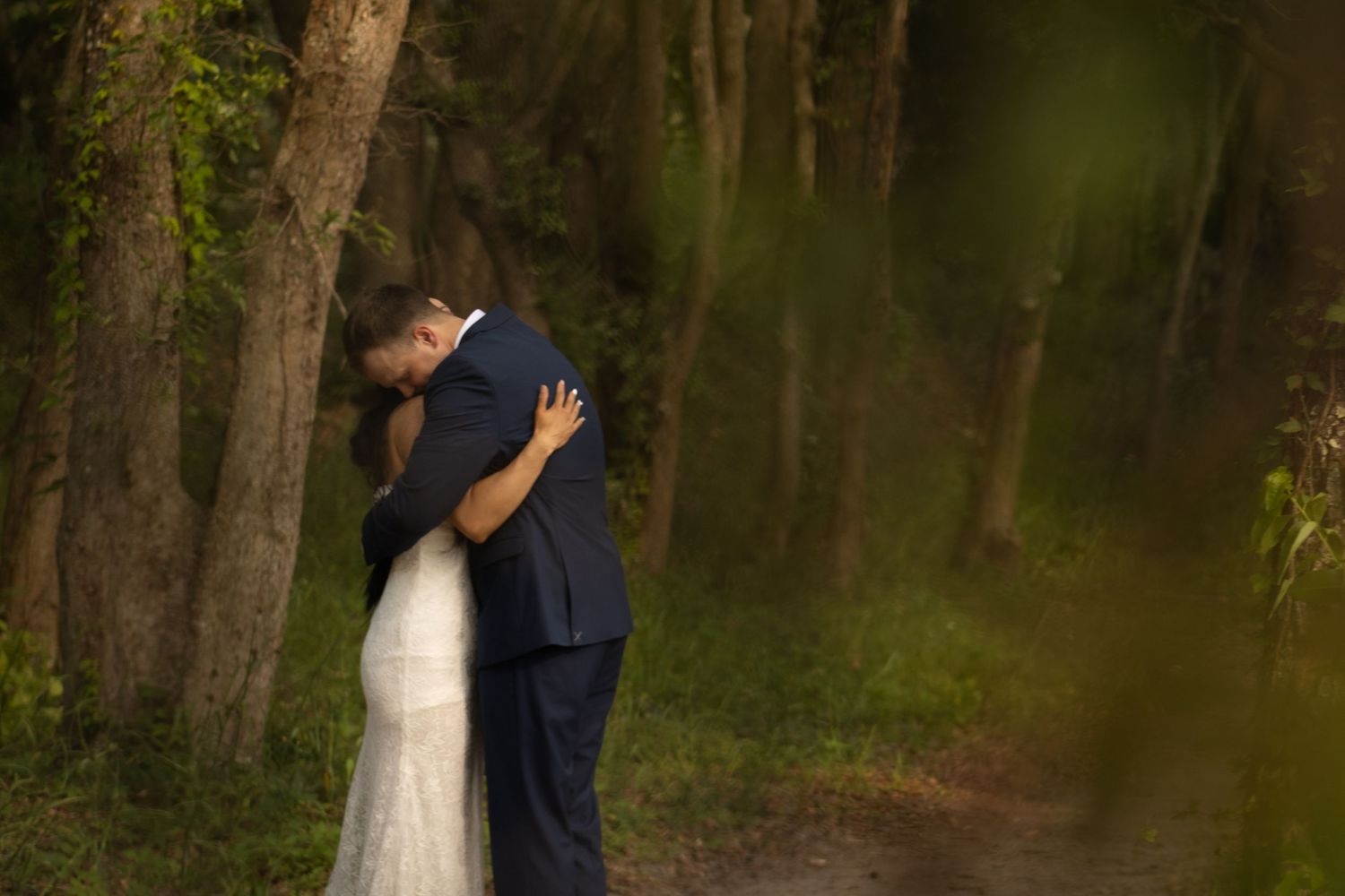 A romantic embrace between newlyweds in a lush forest setting with natural lighting filtering through the trees.