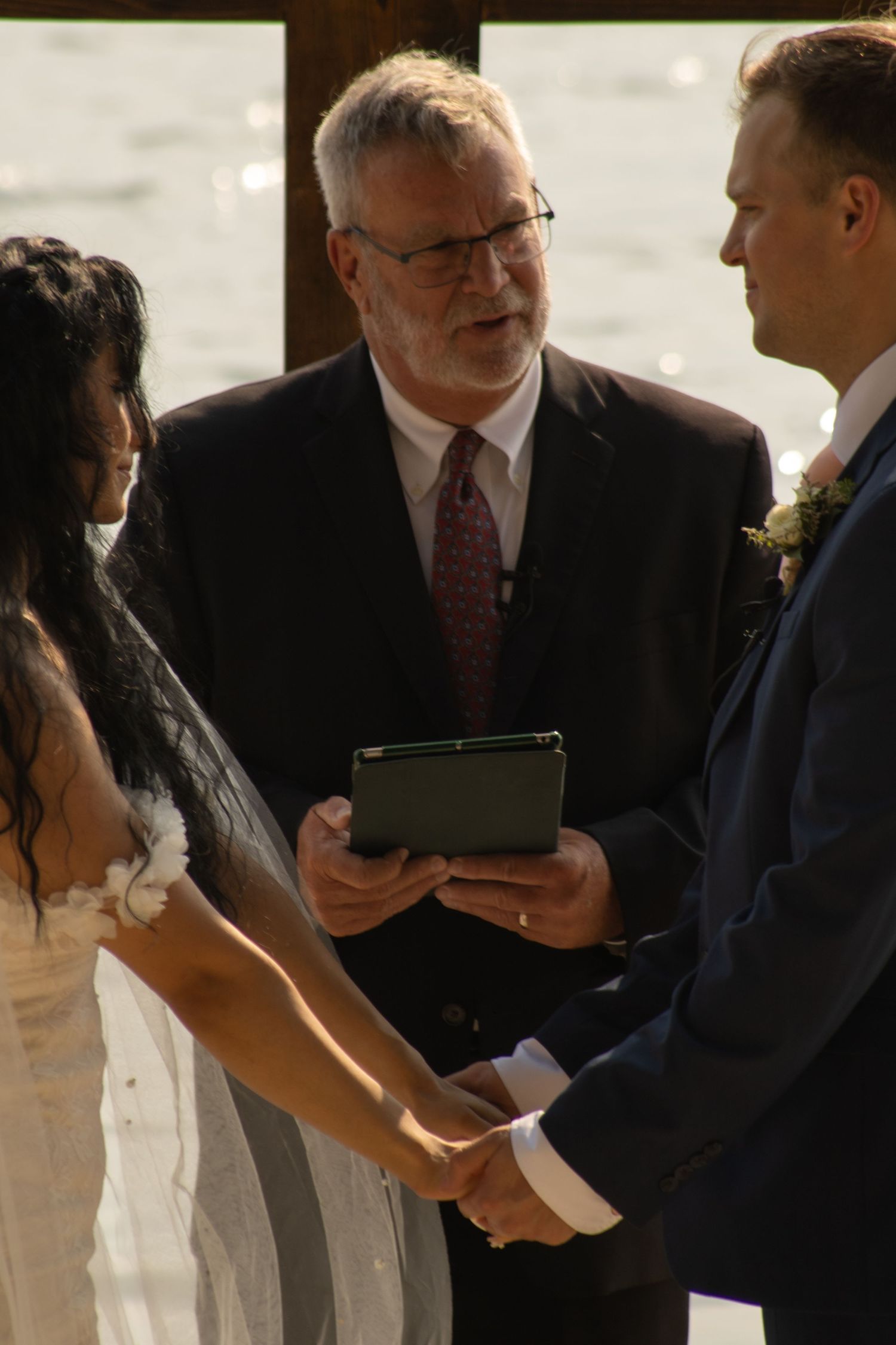 An officiant conducts a wedding ceremony as a couple holds hands at the altar.