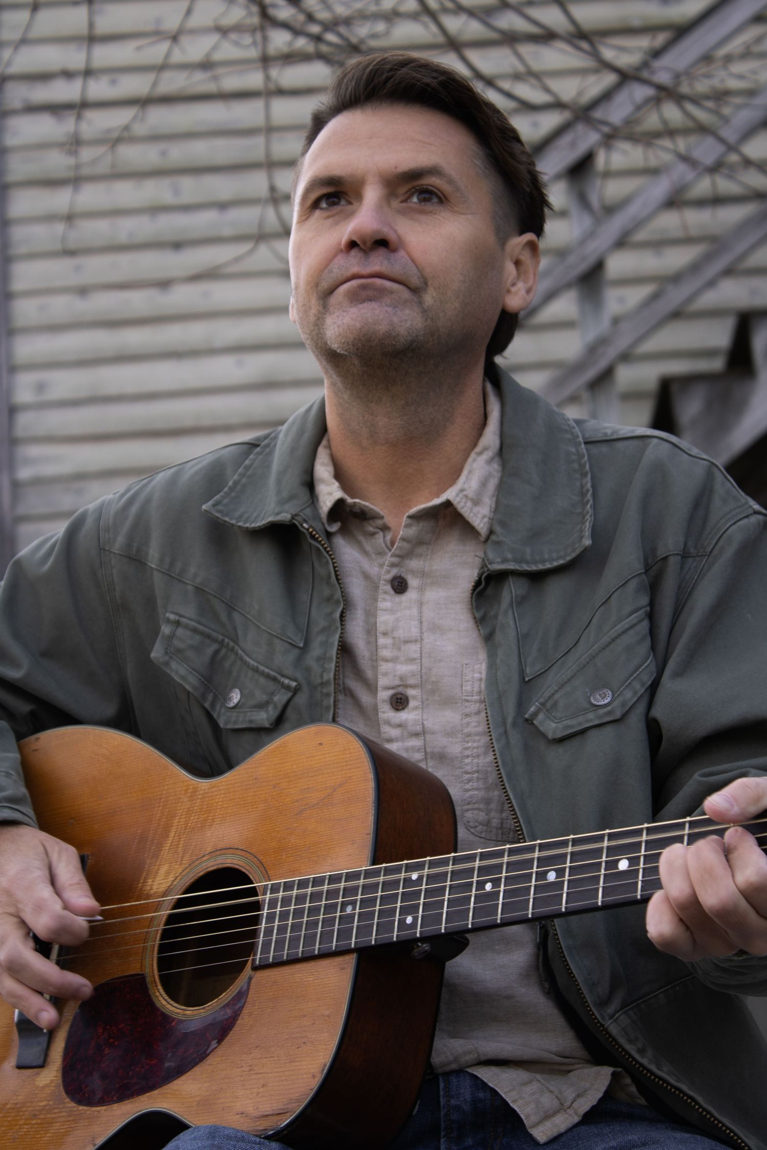 A musician plays an acoustic guitar while wearing a denim jacket outdoors.