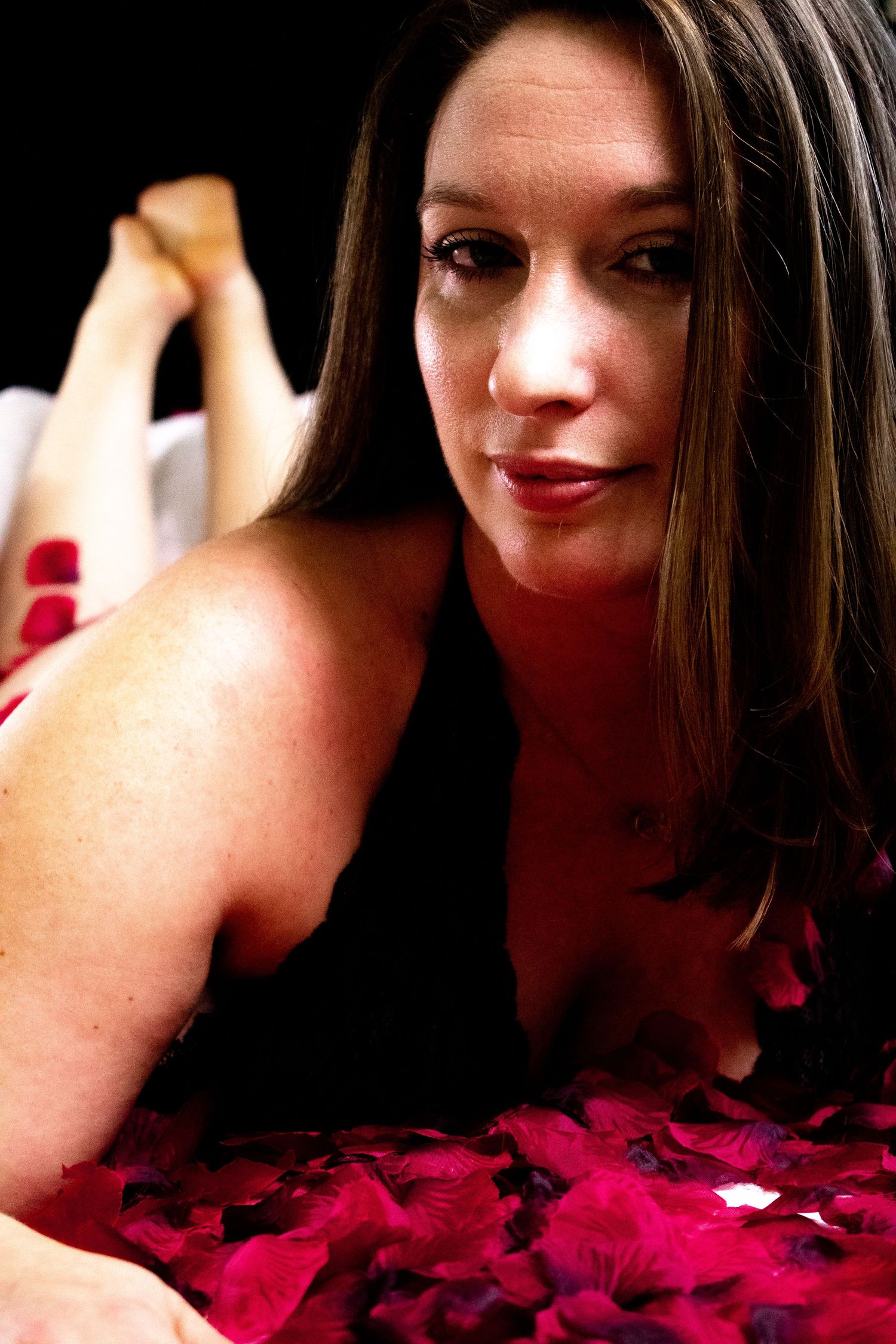 Romantic boudoir photo with red rose petals and dramatic lighting.
