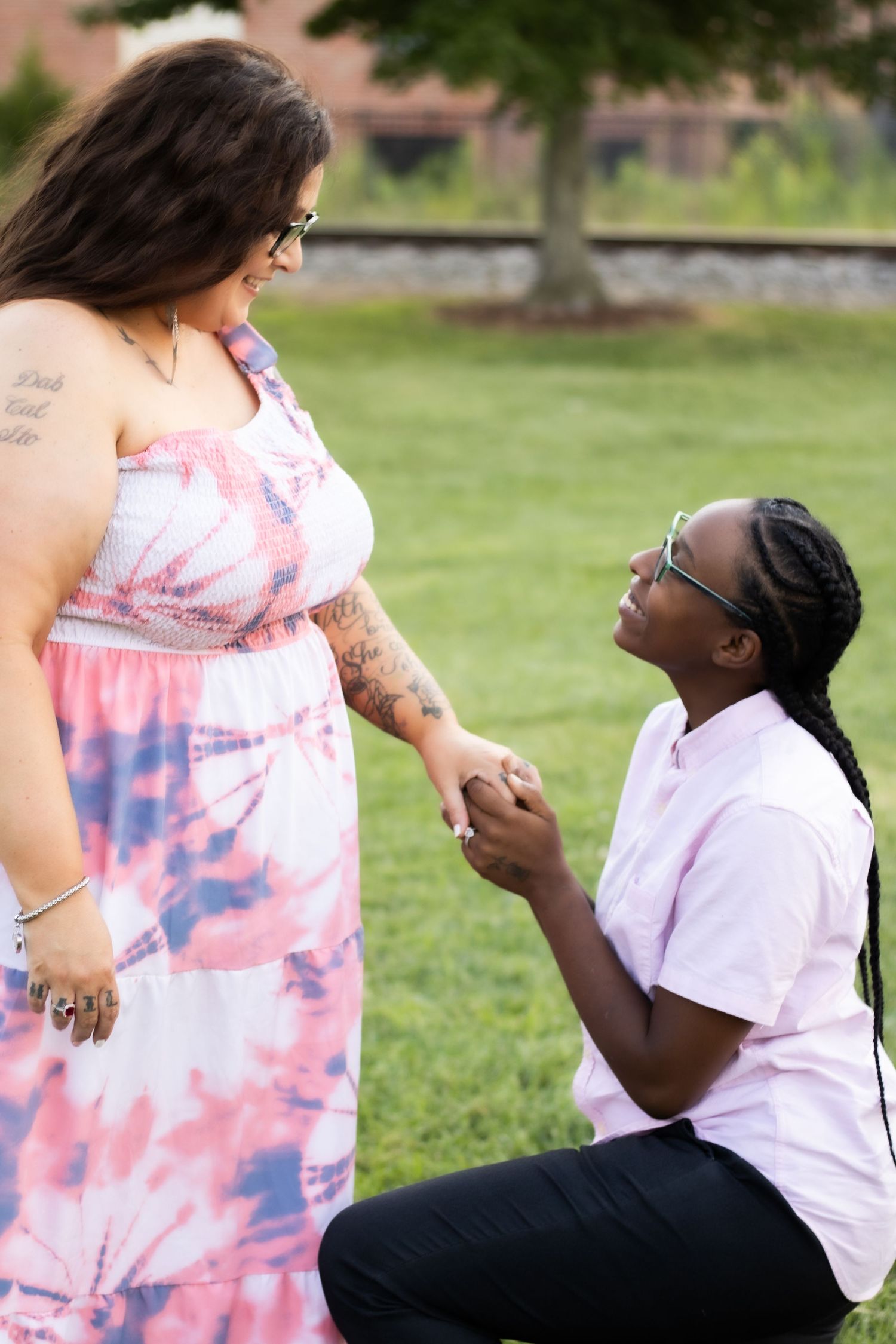 Person in tie-dye dress receiving a marriage proposal in a park setting.