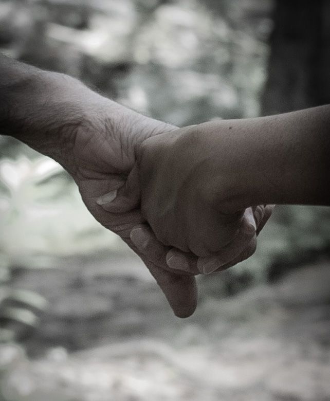 Close-up of hands reaching towards each other against a blurred natural background.
