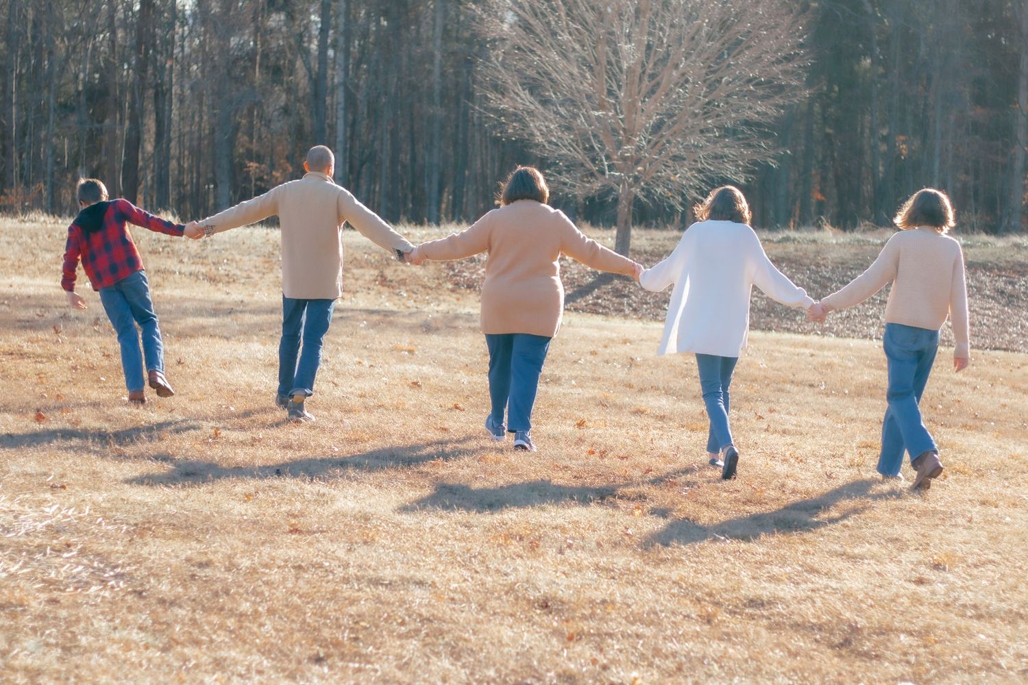 Five people holding hands while walking away on autumn field at sunset.