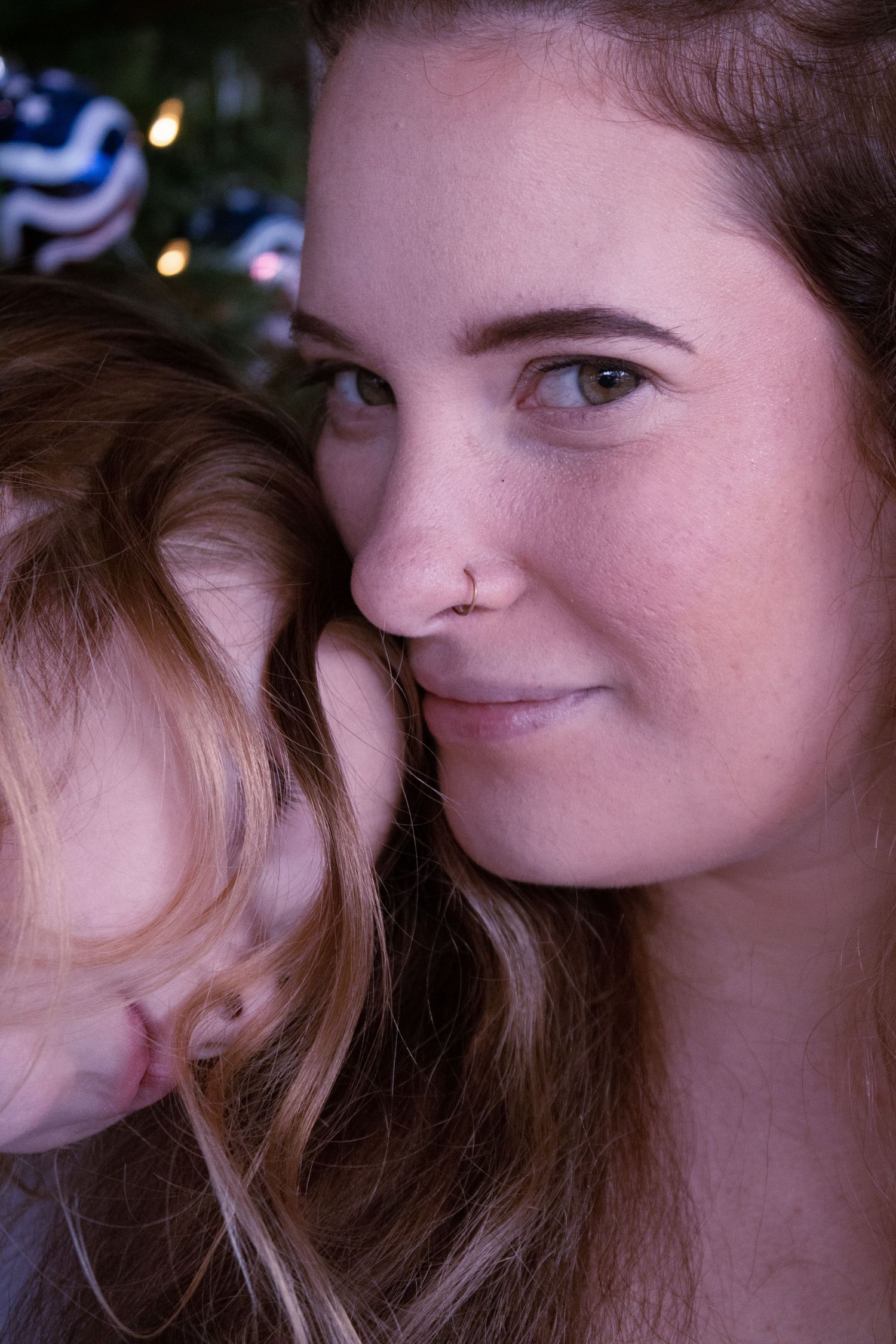 Close-up intimate portrait with soft lighting and holiday decorations in background.