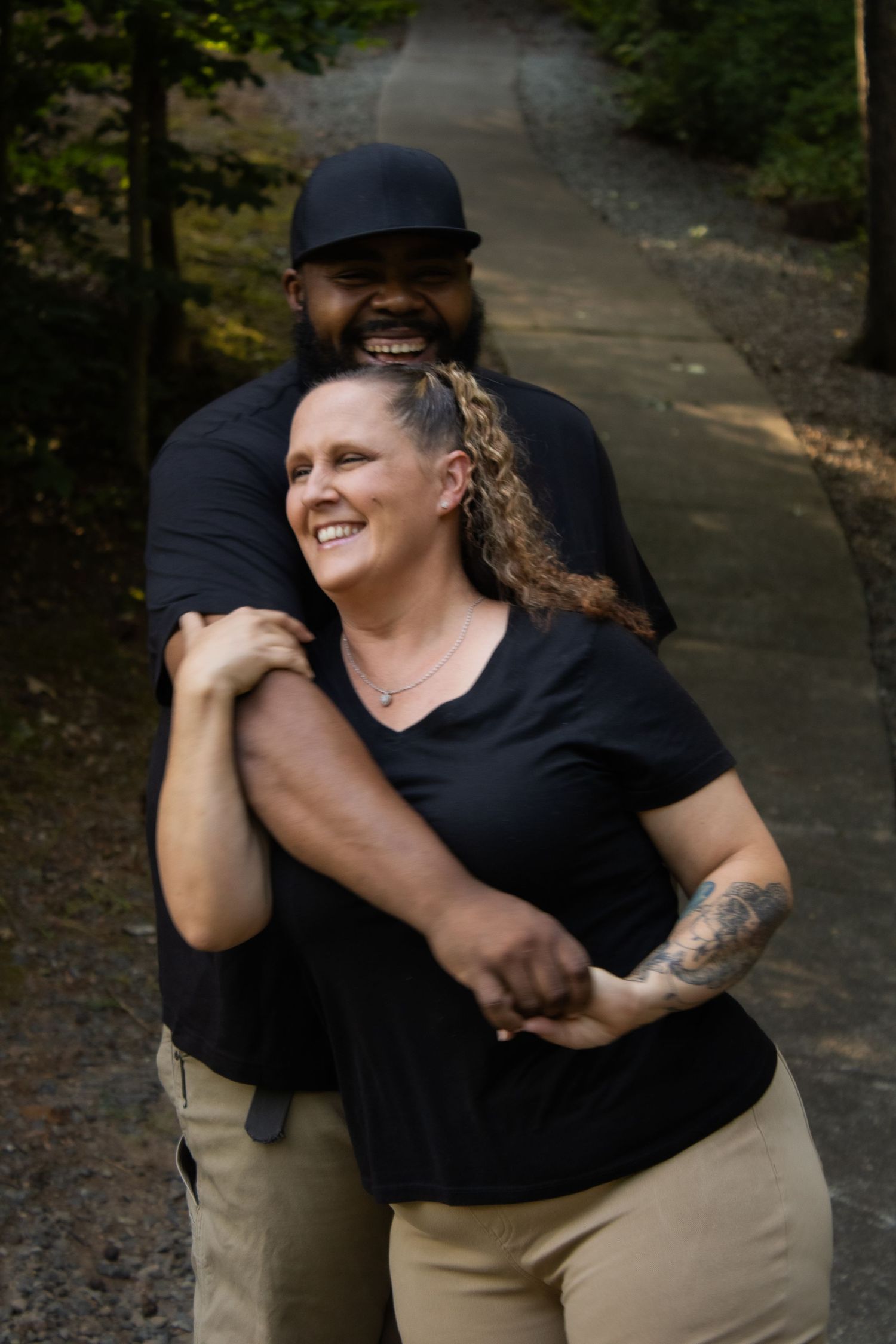 Two people share a playful embrace outdoors while wearing black shirts and khaki pants.