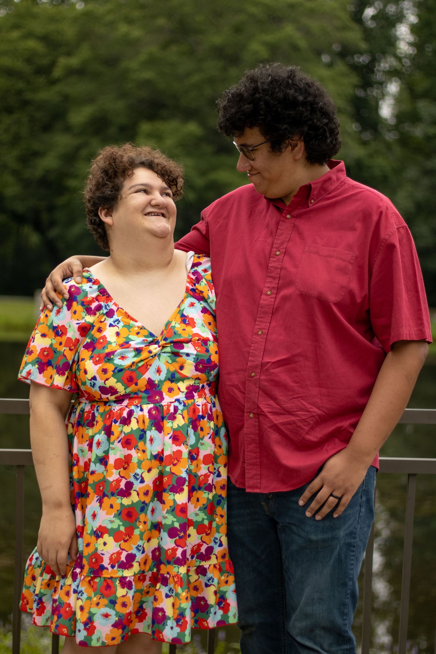 Two people share a joyful moment together on a railing with trees in the background.
