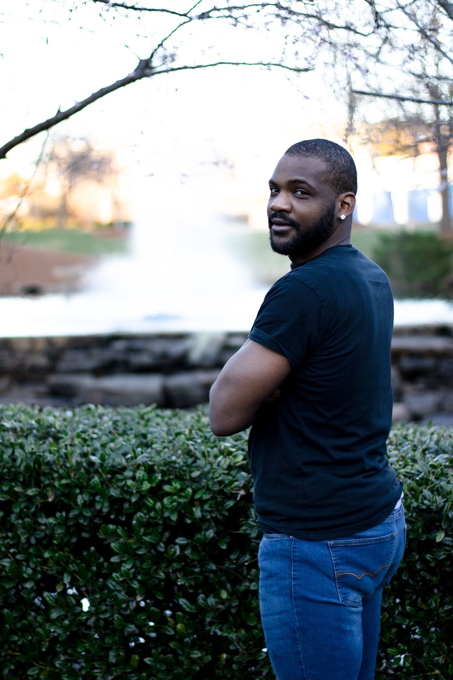 Portrait of a man in a black t-shirt looking over his shoulder at sunset by the water.