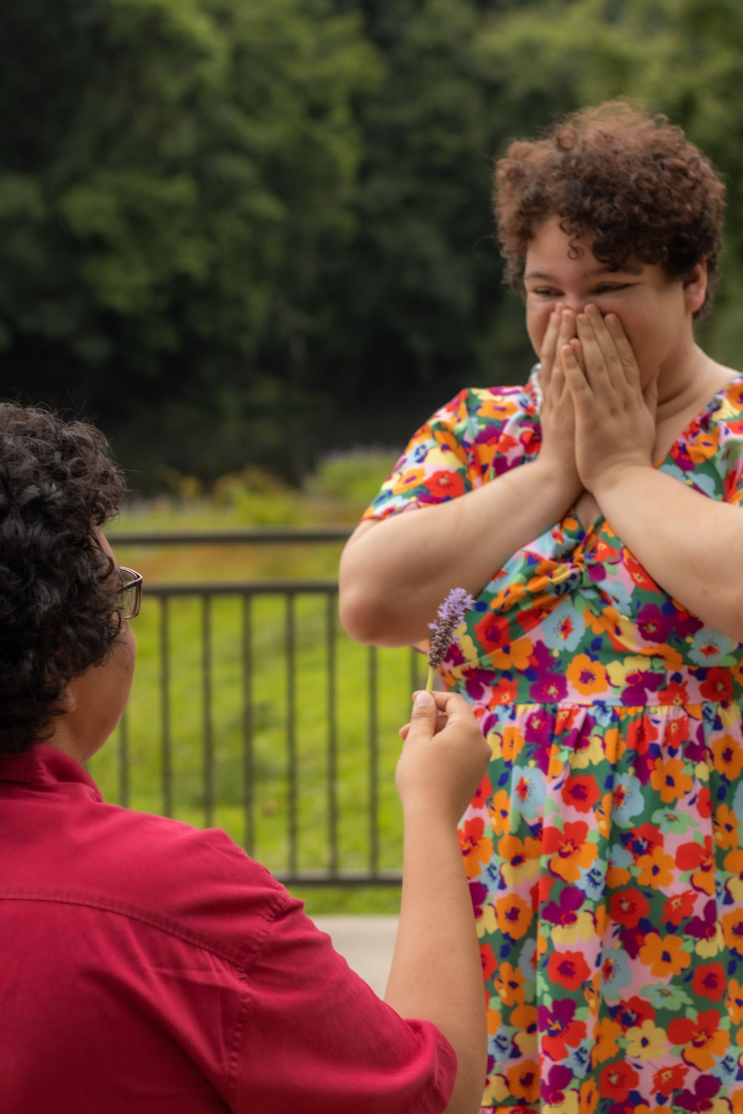 A couple shares an intimate playful moment outdoors wearing a floral dress and red shirt.