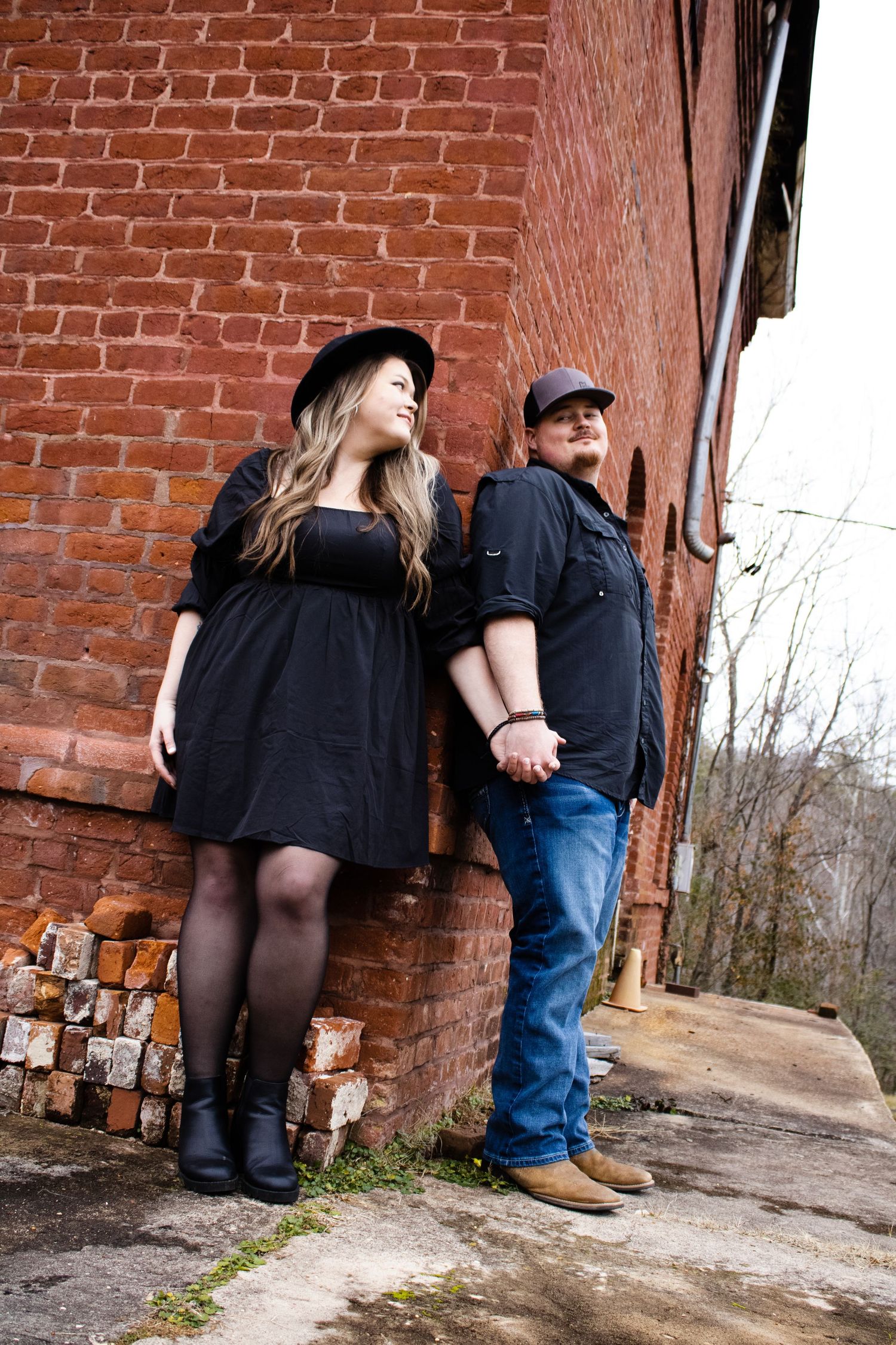 Couple posing against rustic brick wall in casual outfits.