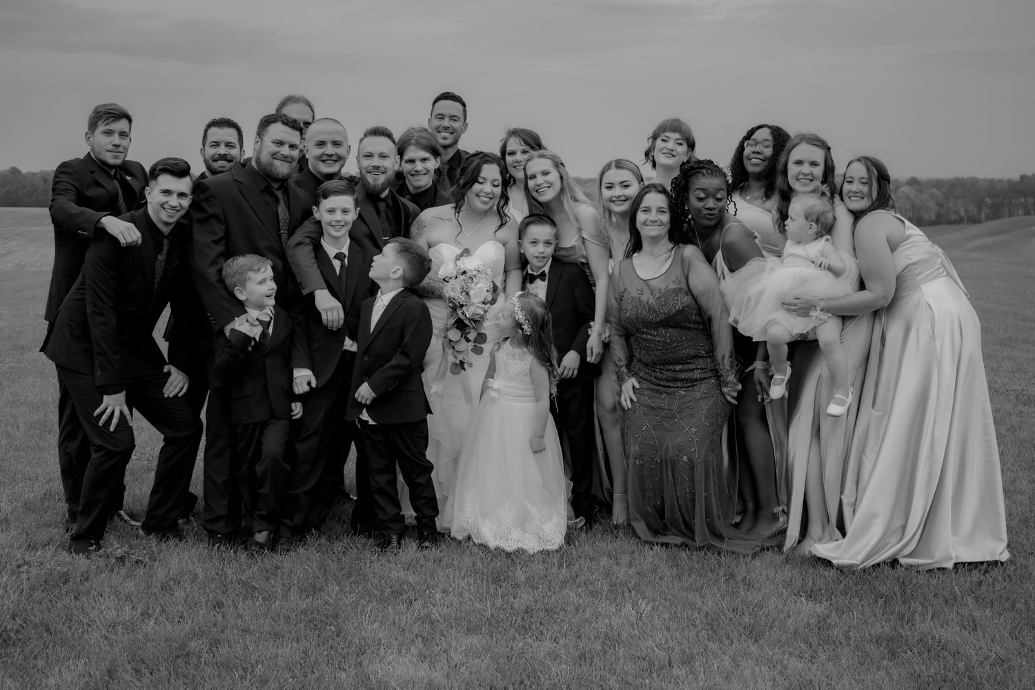 Large wedding party group photo on a hilltop with formal attire in black and white.