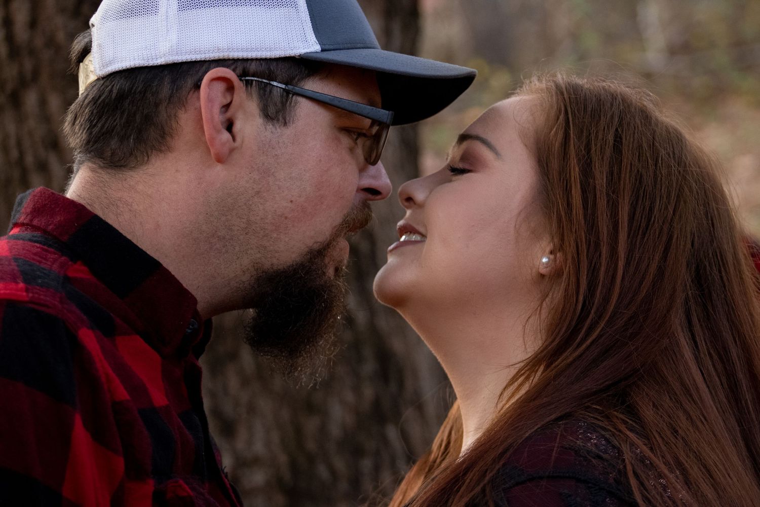 Close-up romantic moment between couple wearing matching red plaid shirts in outdoor setting.