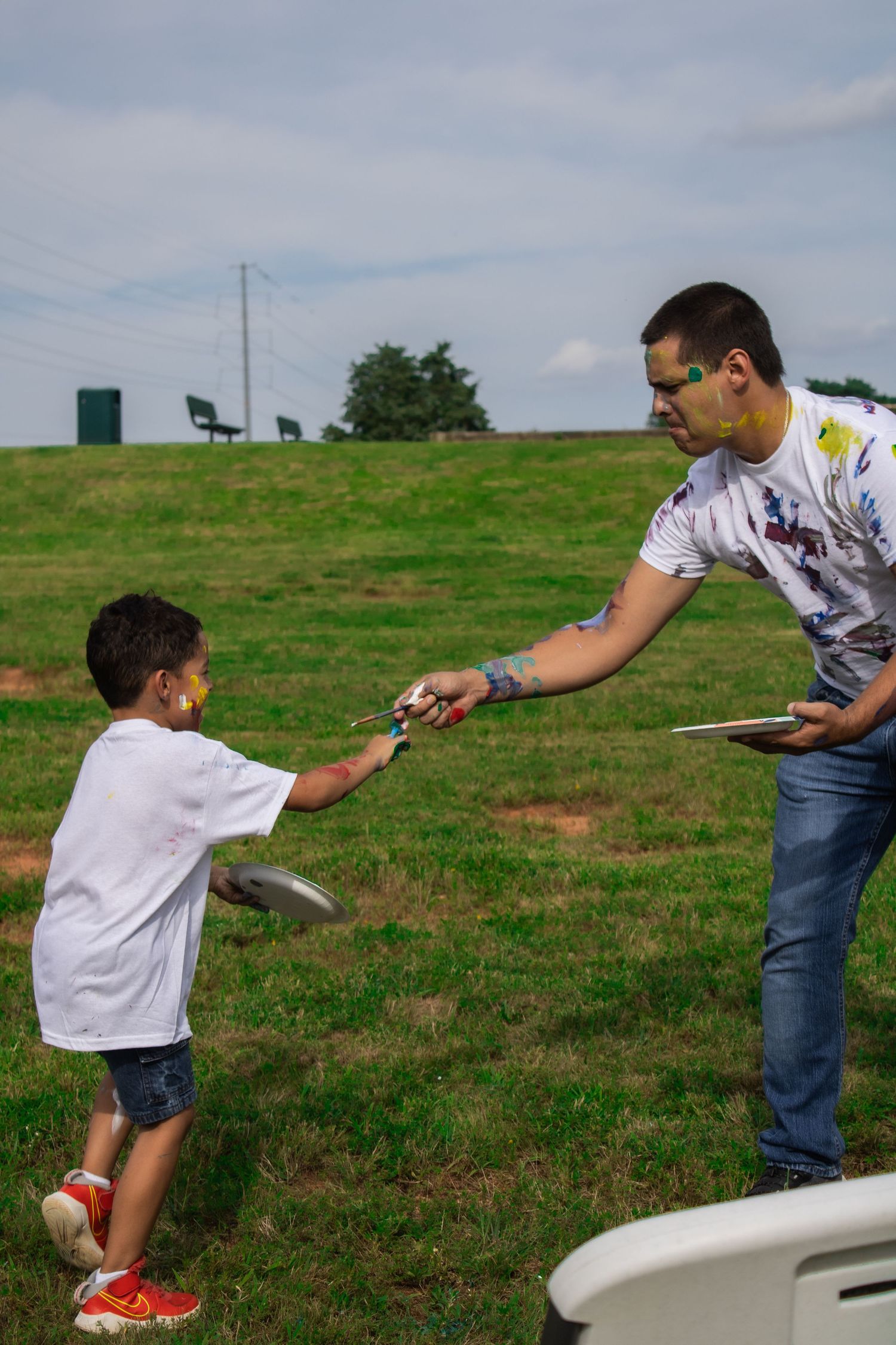 Young child and adult clean paint off themselves outdoors using water.
