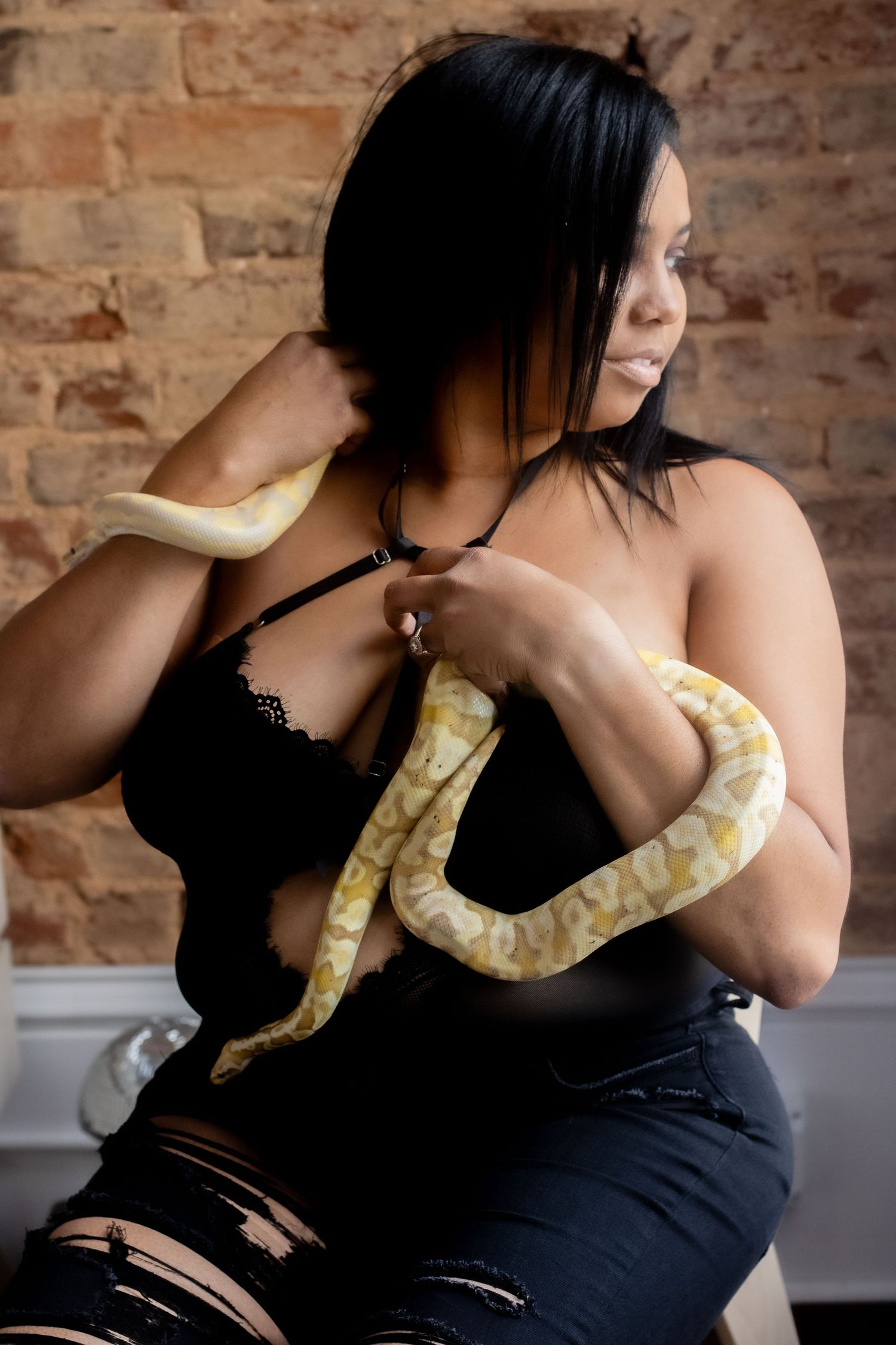 Woman in black outfit posing with an albino python snake against a brick wall background.