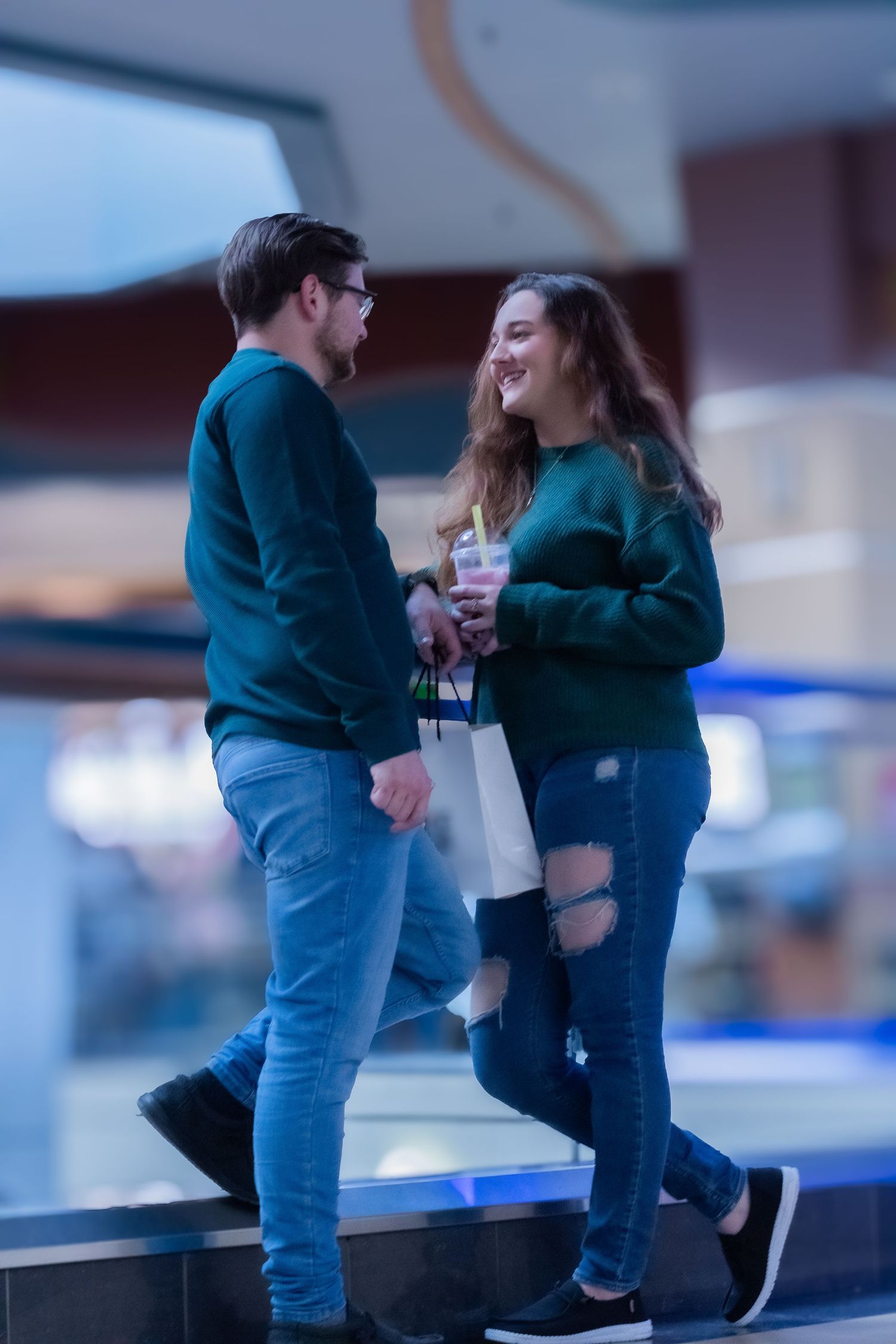 A couple in matching green sweaters sharing a lighthearted moment on steps at night.