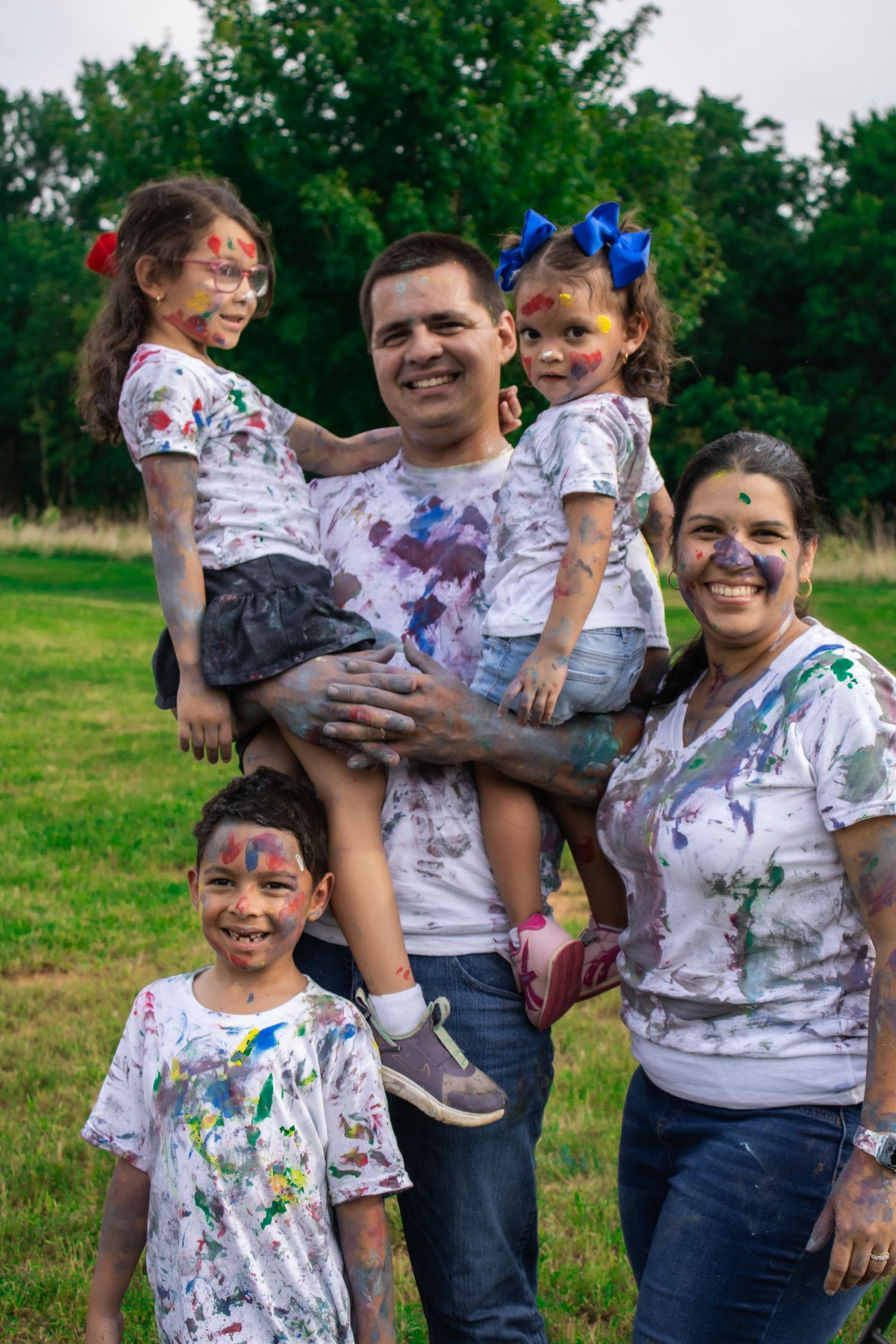 Family shares joyful moments while covered in bright paint during outdoor photoshoot.