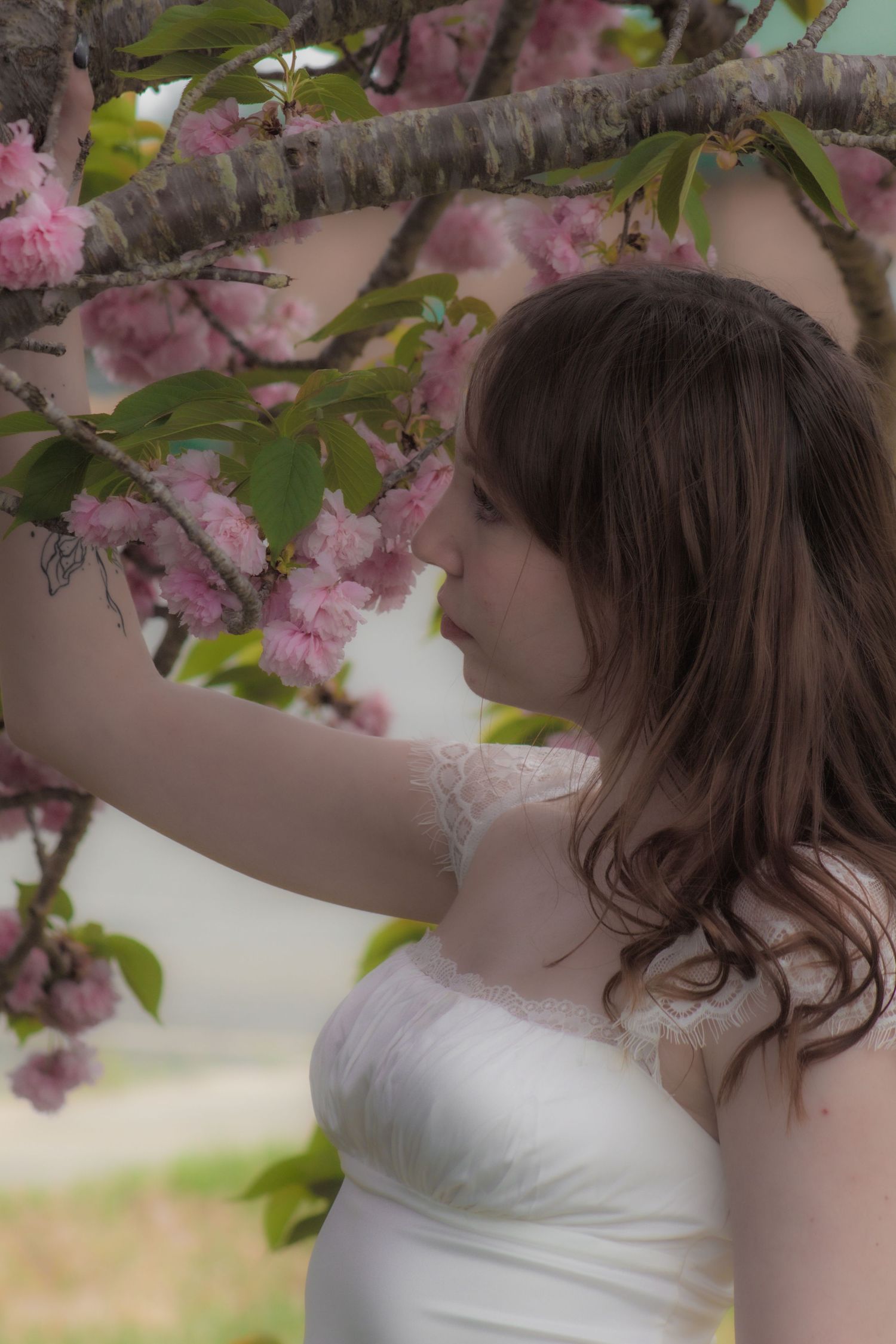 Woman in white dress reaching up to touch pink cherry blossoms in spring.