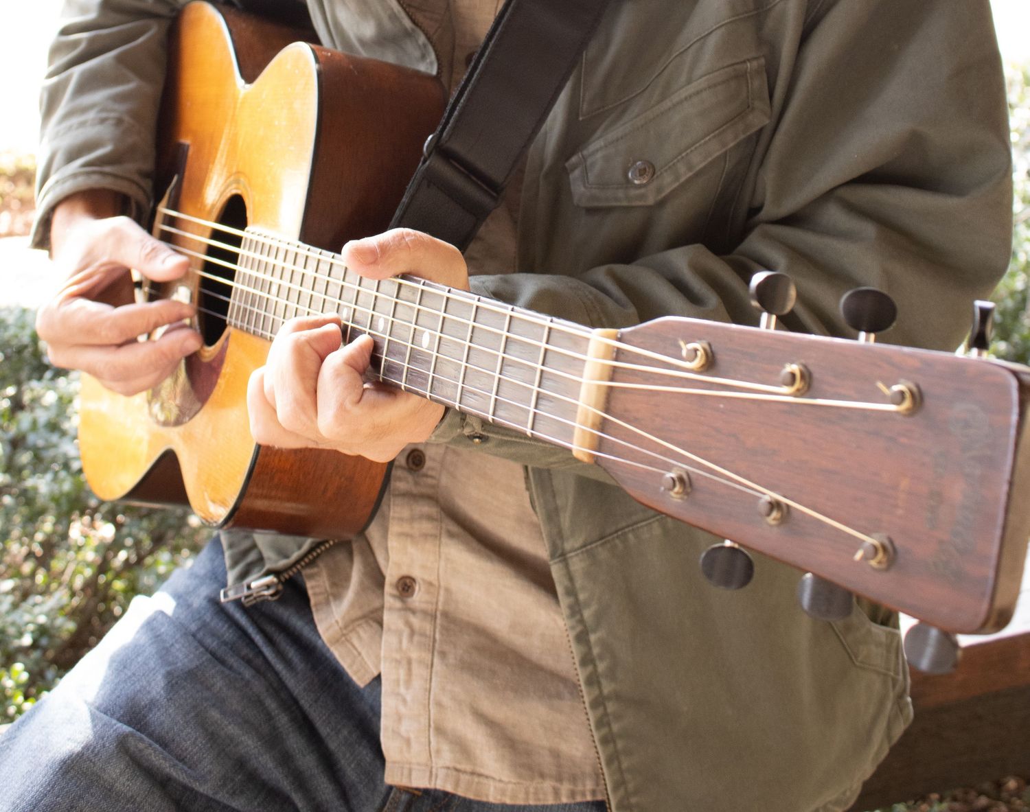 Close-up shot of hands playing an acoustic guitar while wearing a tan jacket.