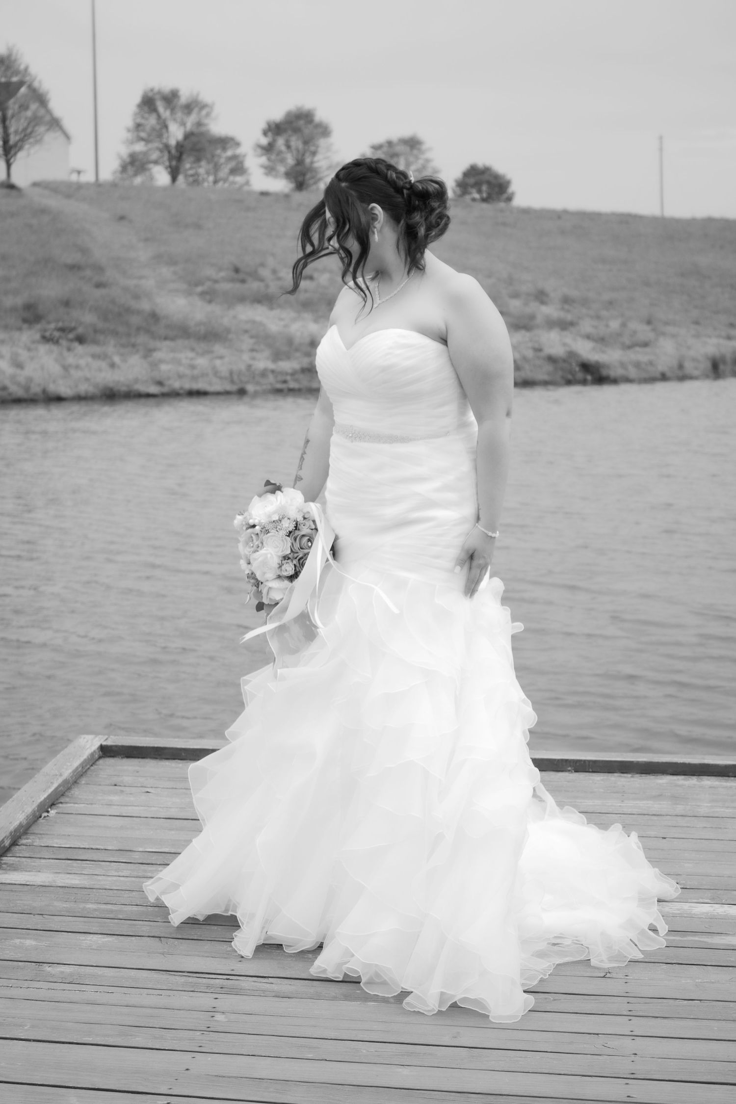 Black and white photo of bride in flowing wedding dress on wooden dock.