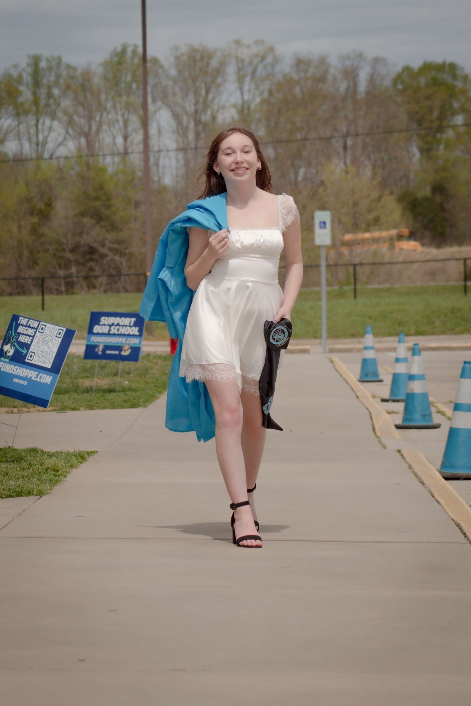 A person in a white dress walking on a sidewalk carrying a blue jacket and purse.