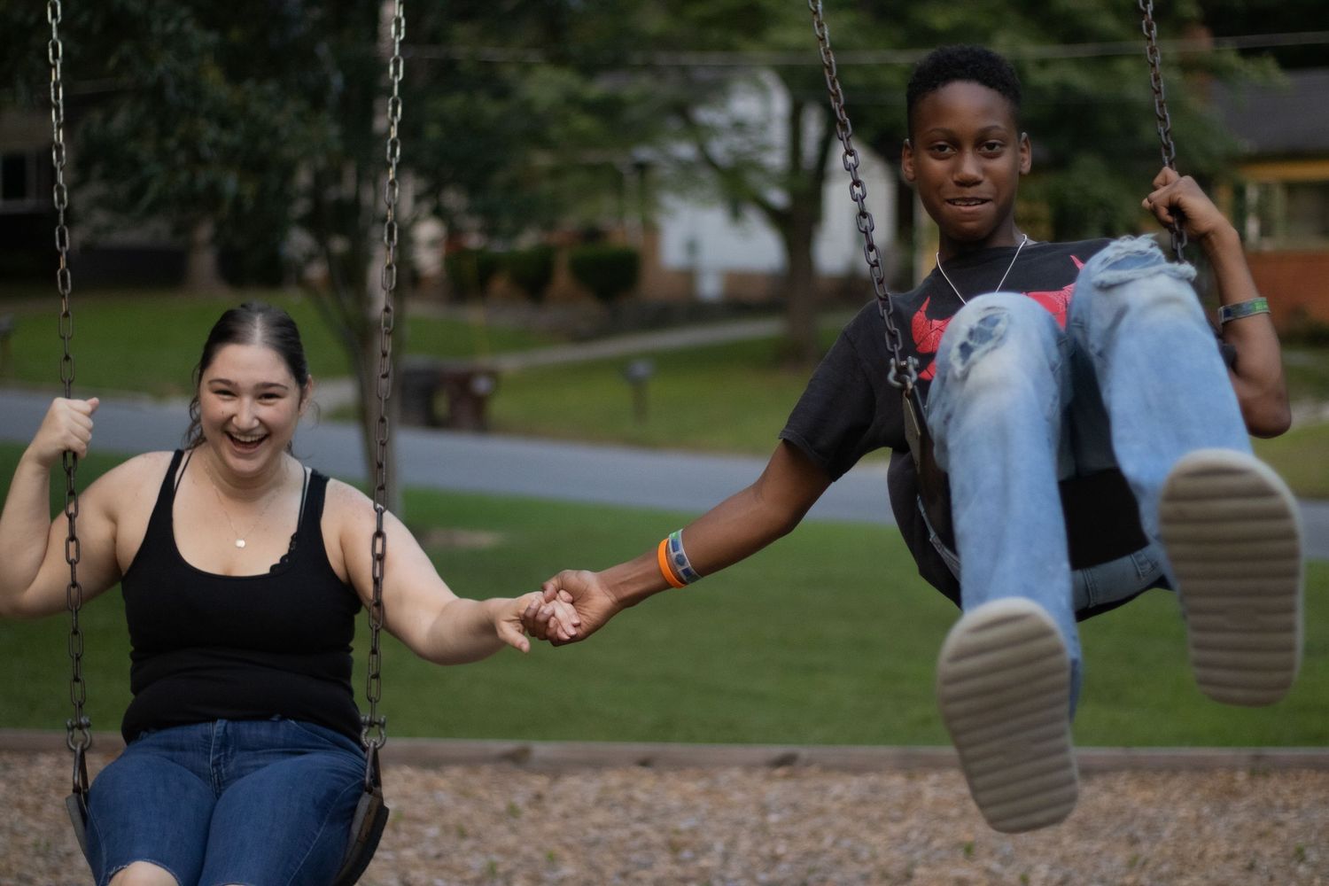 Friends laugh while swinging together at a park playground.