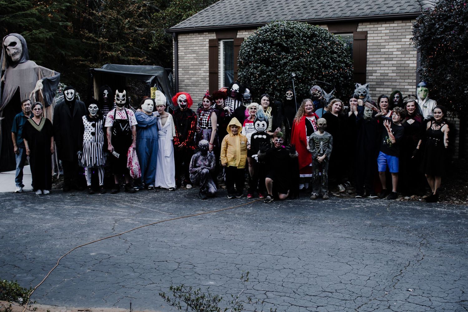 Large group in Halloween costumes gathered outside brick building for group photo.
