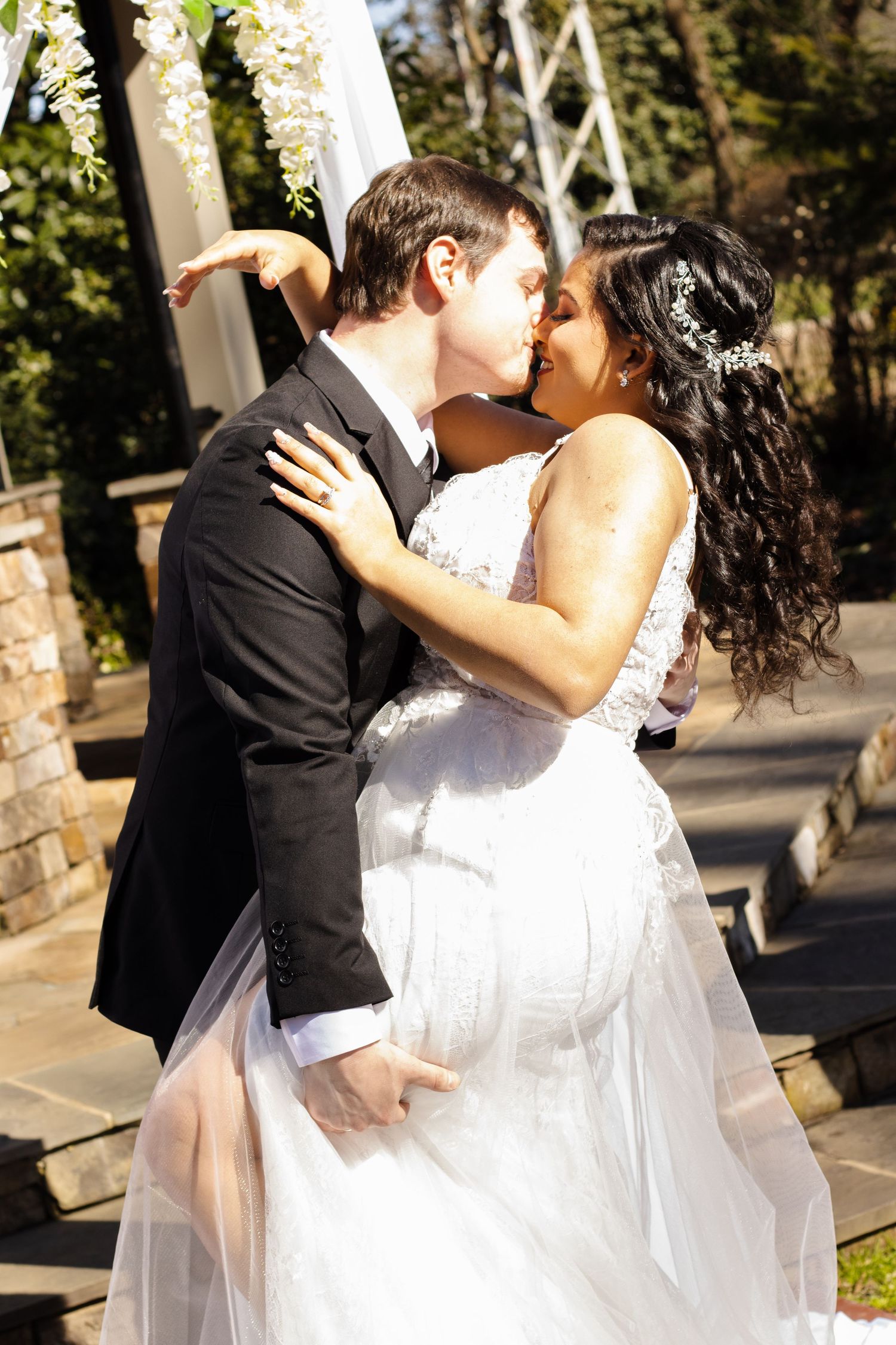 A tender wedding moment captured as the couple embraces under an outdoor arch.