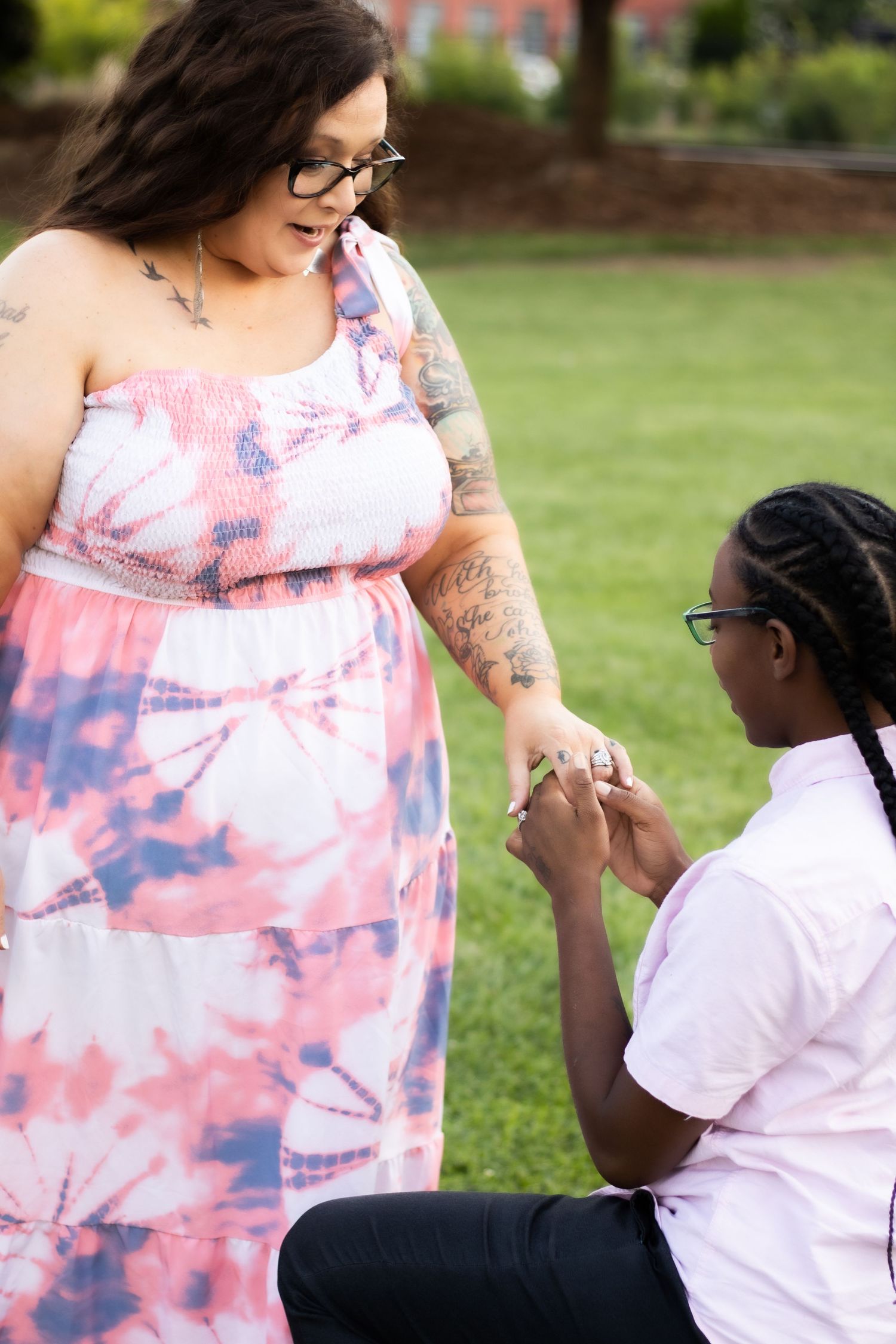 Outdoor proposal scene with person in tie-dye dress receiving ring from kneeling partner.