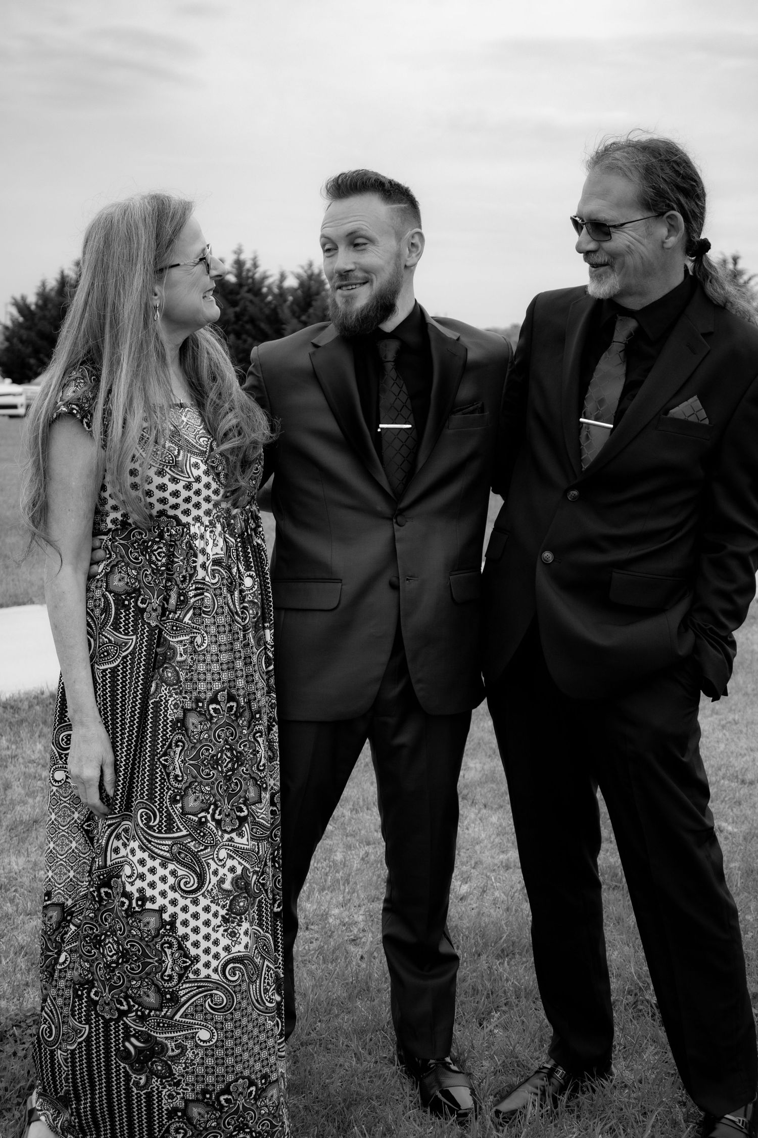 Black and white outdoor portrait of three formally dressed wedding guests.