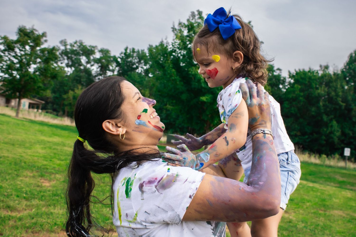 Family plays with colorful paints outdoors on a grassy field during a fun photoshoot.