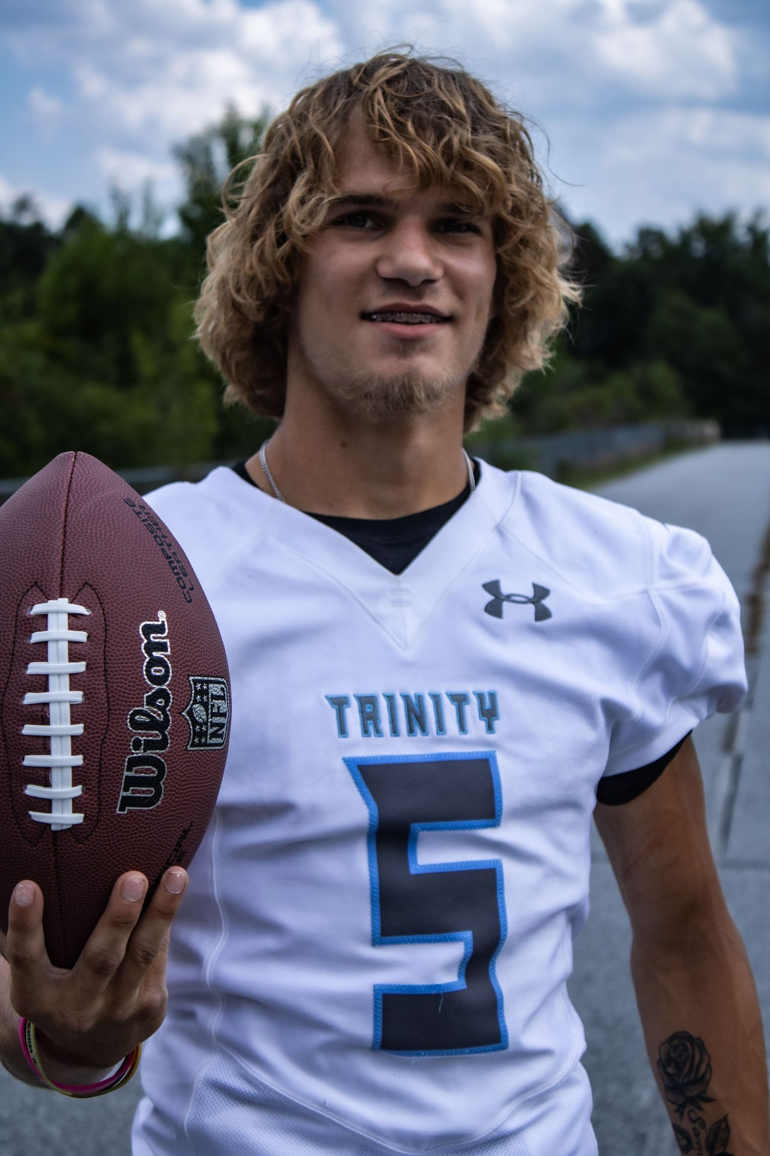 Trinity football player in white jersey number 5 holds ball while standing outdoors.