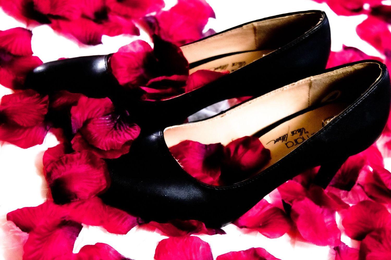 Black dress shoes arranged on scattered red rose petals.