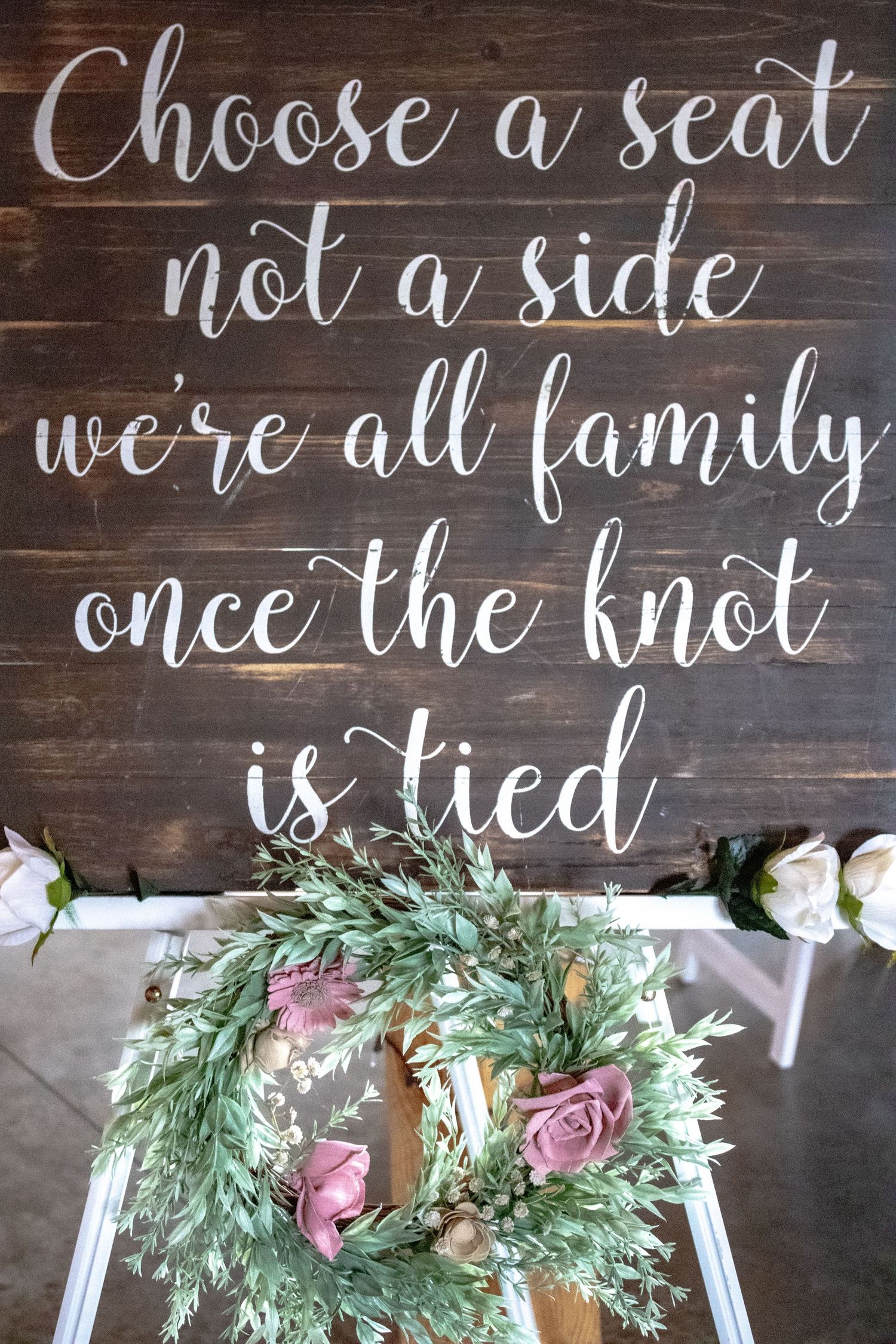 Rustic wooden wedding sign with calligraphy text and floral decorations.