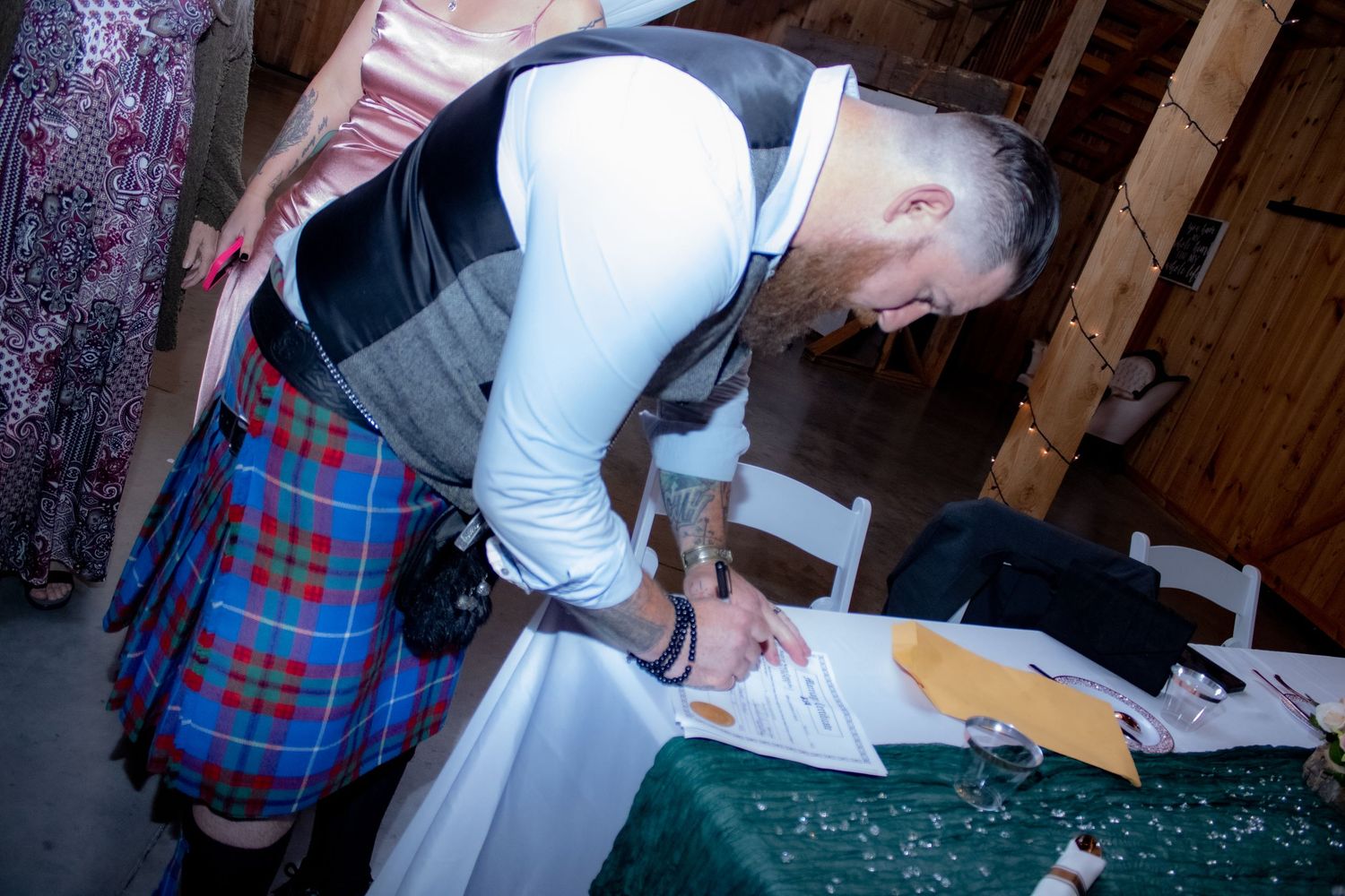 Wedding signing ceremony with traditional Scottish kilt details in rustic setting.