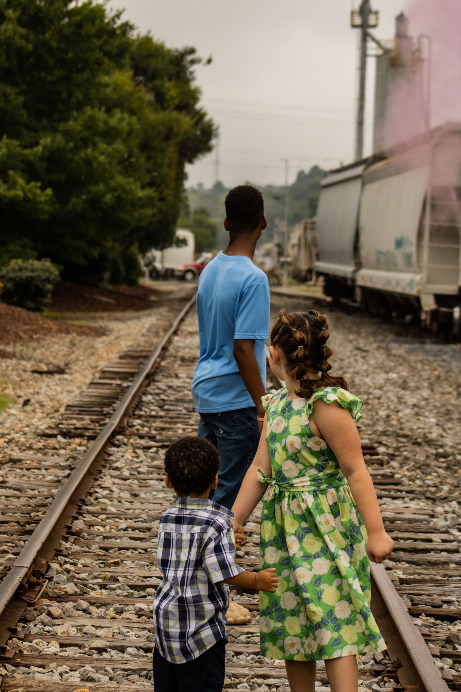 Two children walk together along railroad tracks in casual clothing.