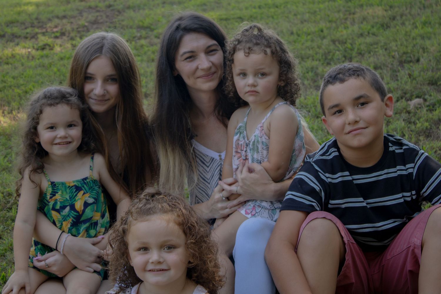 Group portrait of family members sitting together outdoors on a grassy slope.