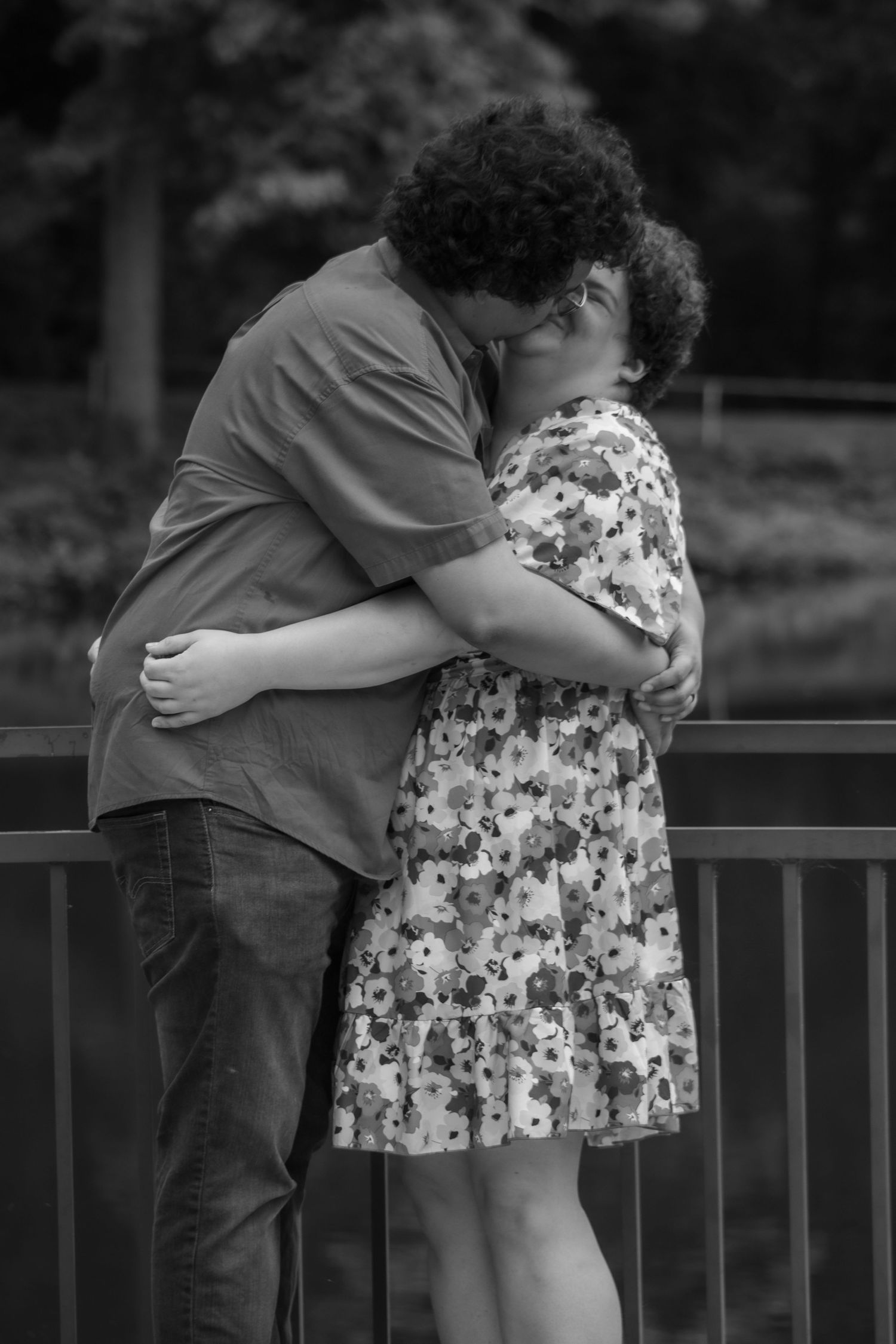 Black and white photo of a couple sharing an intimate embrace on a bridge.