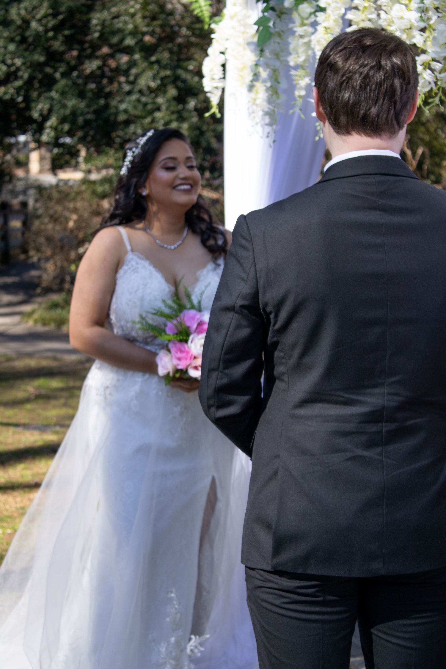Wedding couple shares intimate moment outdoors with bride in flowing white dress.