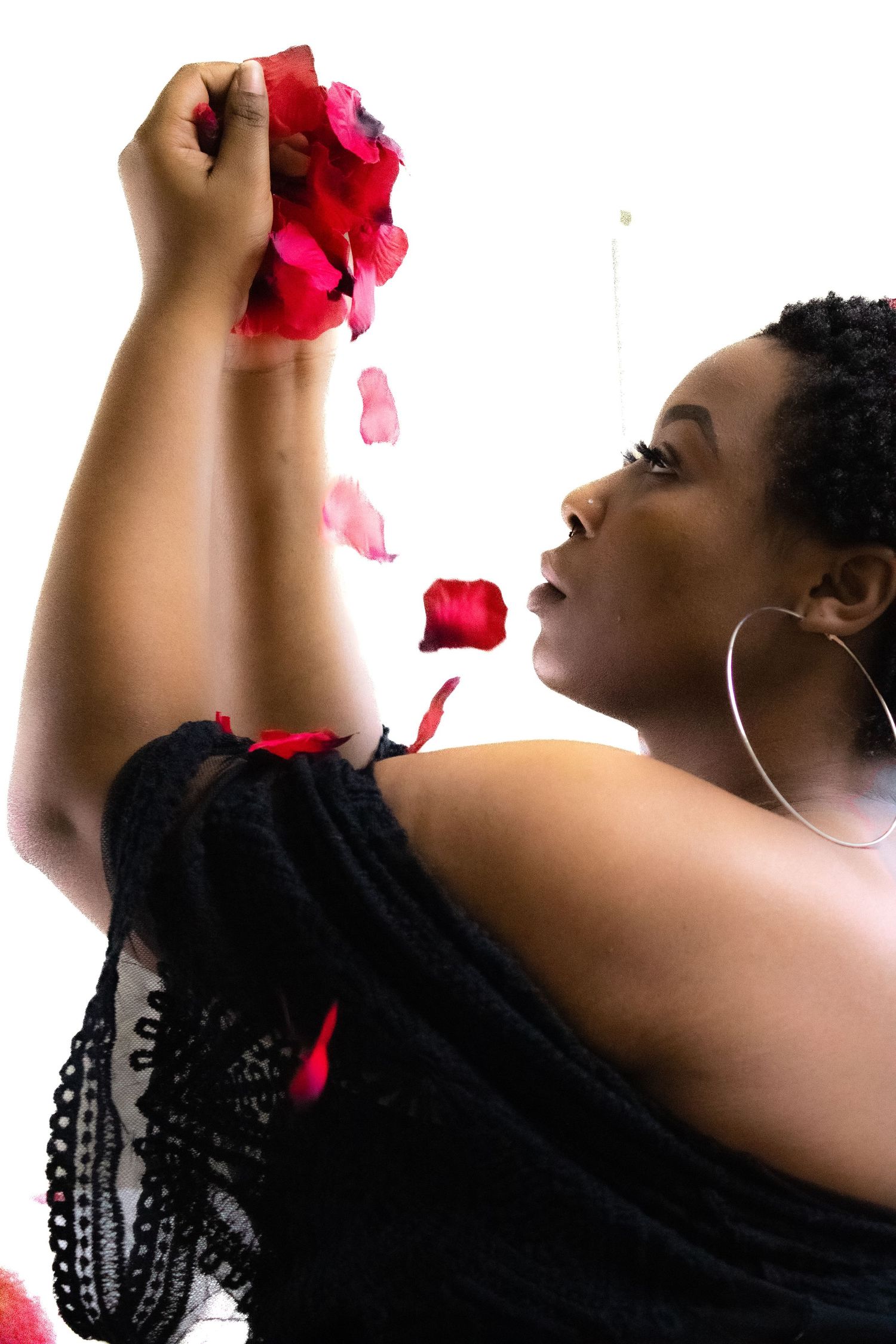Figure in black tossing red rose petals in artistic motion against white background.