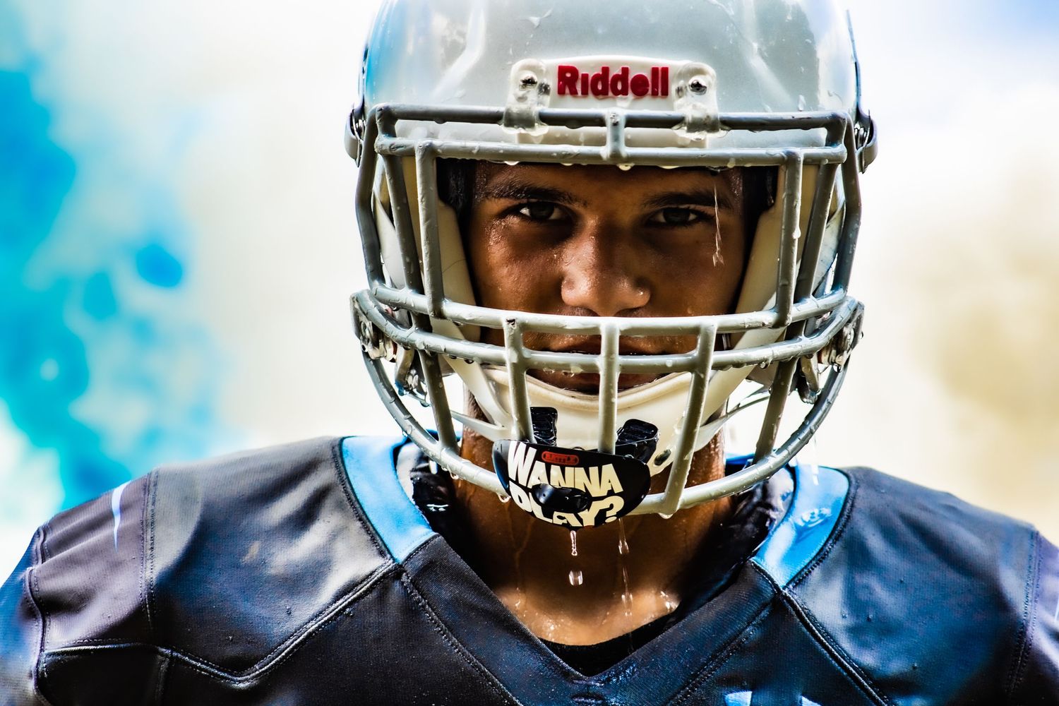 Football player wearing a silver Riddell helmet against a bright blue sky background.