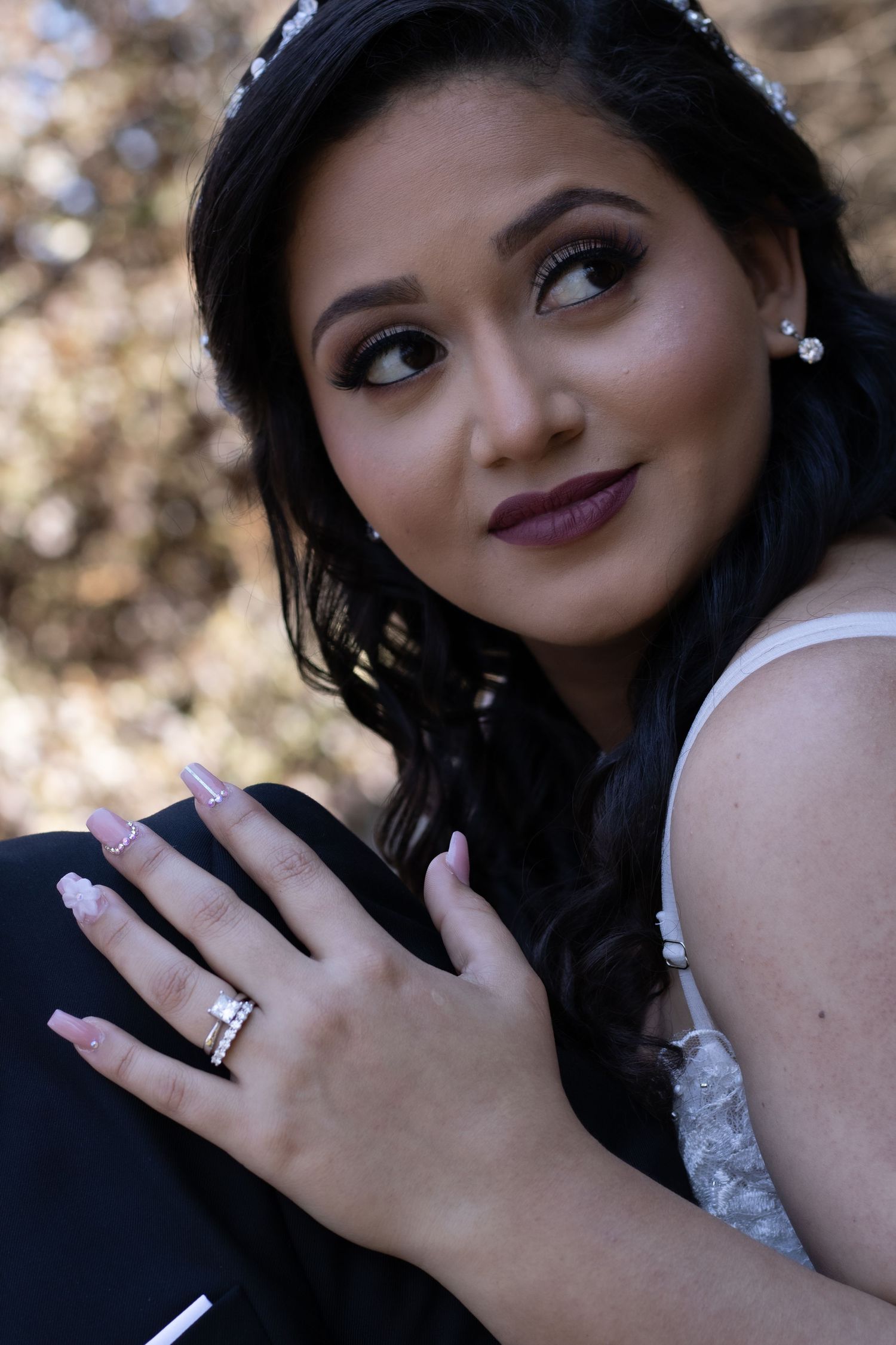 Elegant bridal portrait featuring dark lipstick, pearl earrings and a wedding ring against a soft bokeh background.