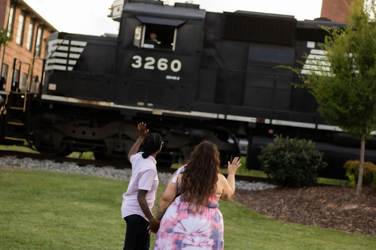 Couple walking away from a black train engine in a grassy area.