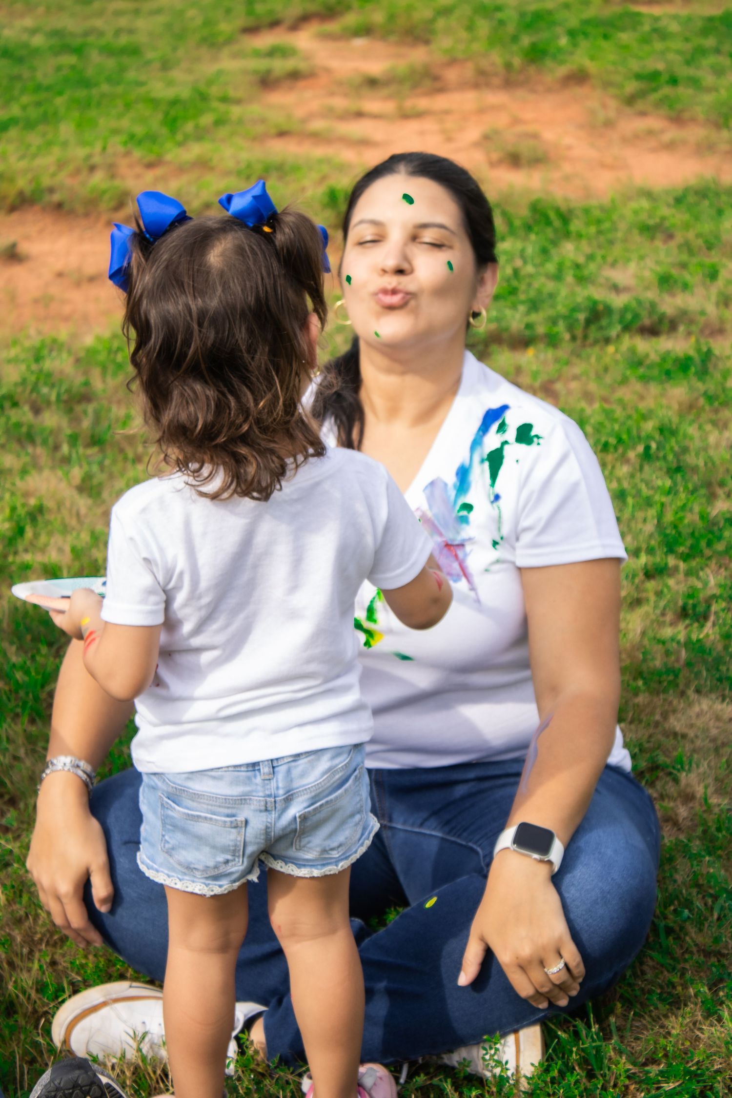 Parent and child share tender moments while sitting in grass during paint activity.